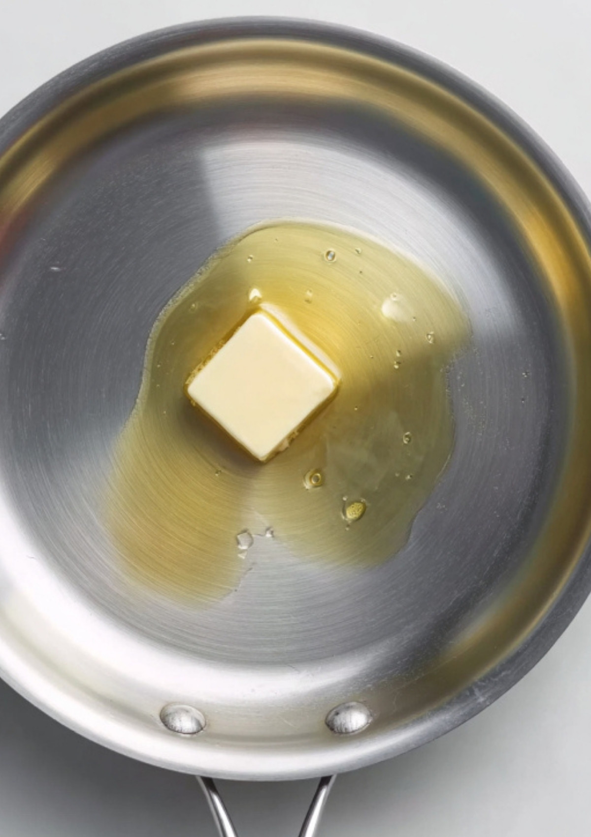 A square pat of butter melting in a stainless steel skillet to begin the base of a veal scallopini sauce recipe.