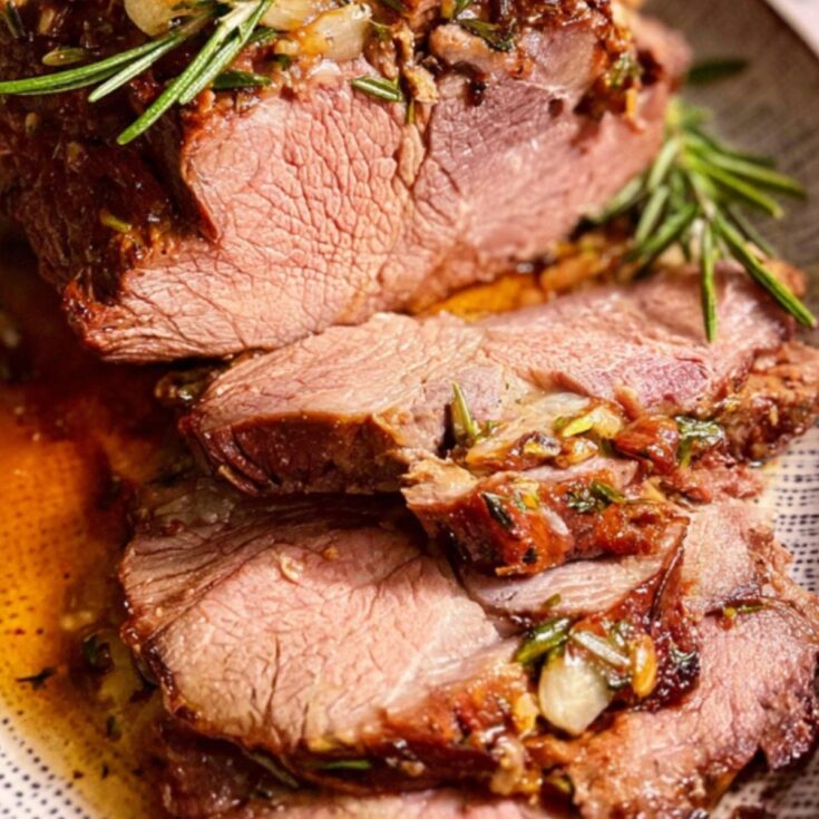 A beautifully carved Chuck Tender Roast showing its internal texture, garnished with fresh rosemary and pan drippings.