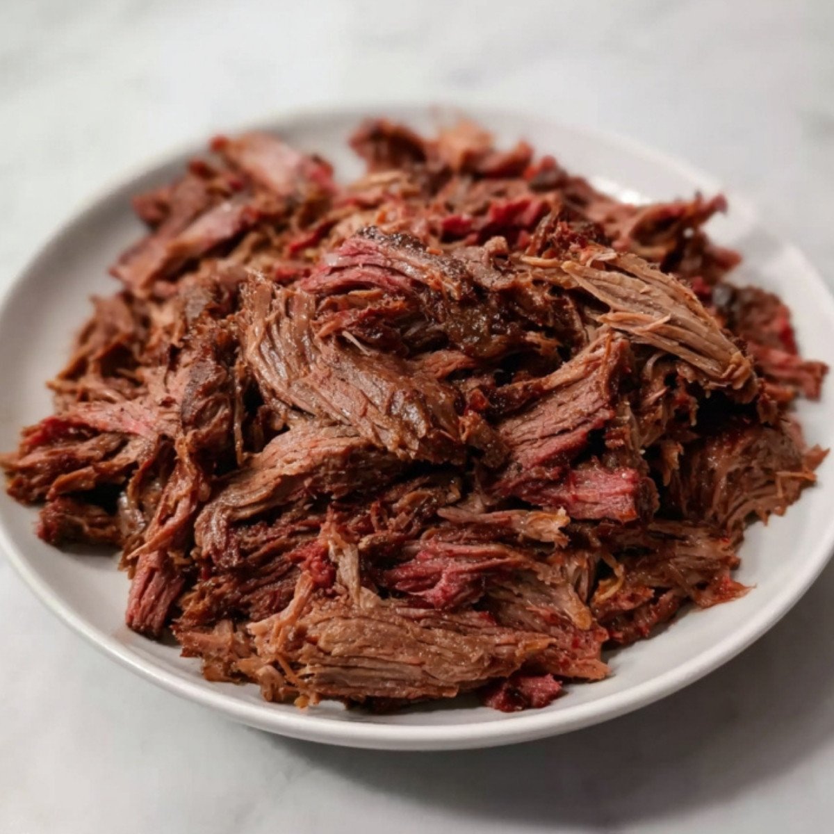 A white plate piled high with succulent, shredded smoked beef chuck roast ready to be served.