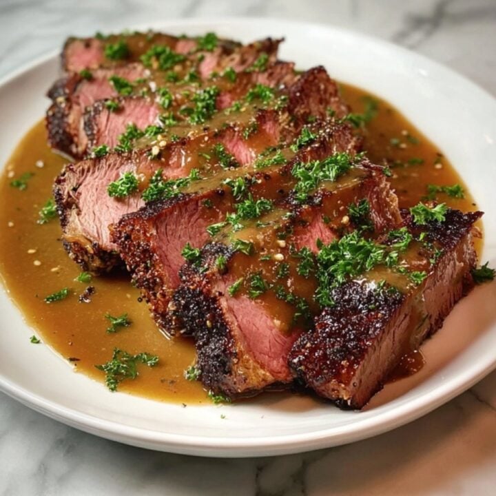 A beautiful final presentation of sliced, fork-tender chuck roast served with a savory reduction and fresh herbs on a white platter.