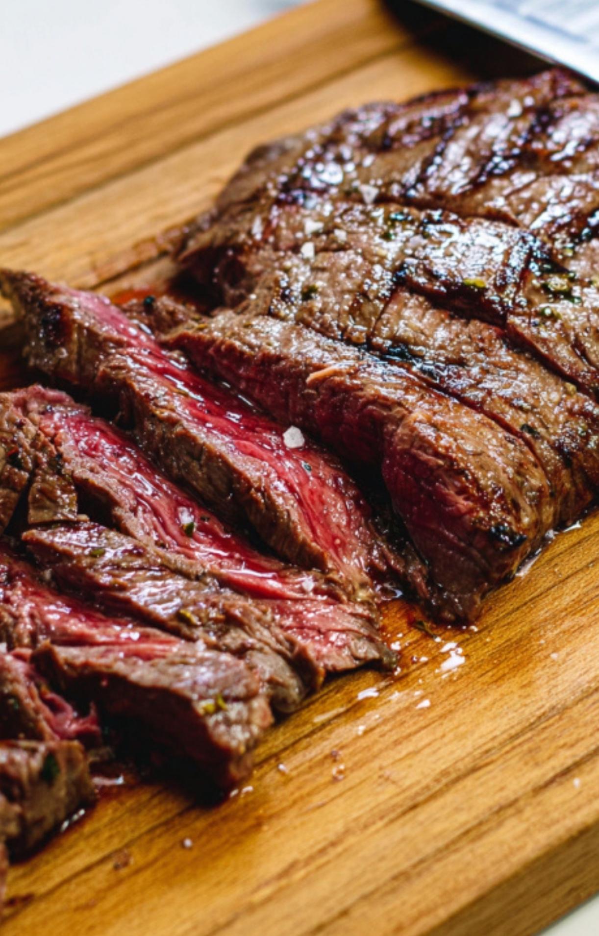 Slices of medium-rare grilled skirt steak on a wooden cutting board, juicy and ready to be served with chimichurri sauce.