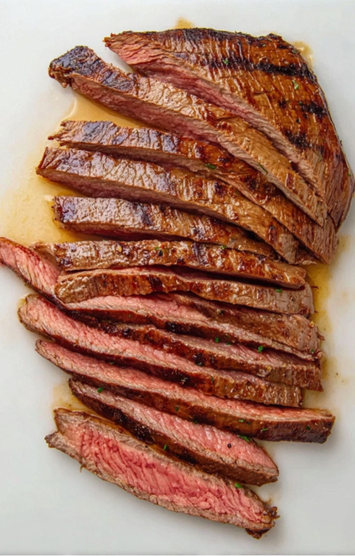 Thinly sliced grilled flank steak on a white cutting board, showing juicy, medium-rare beef with charred edges.