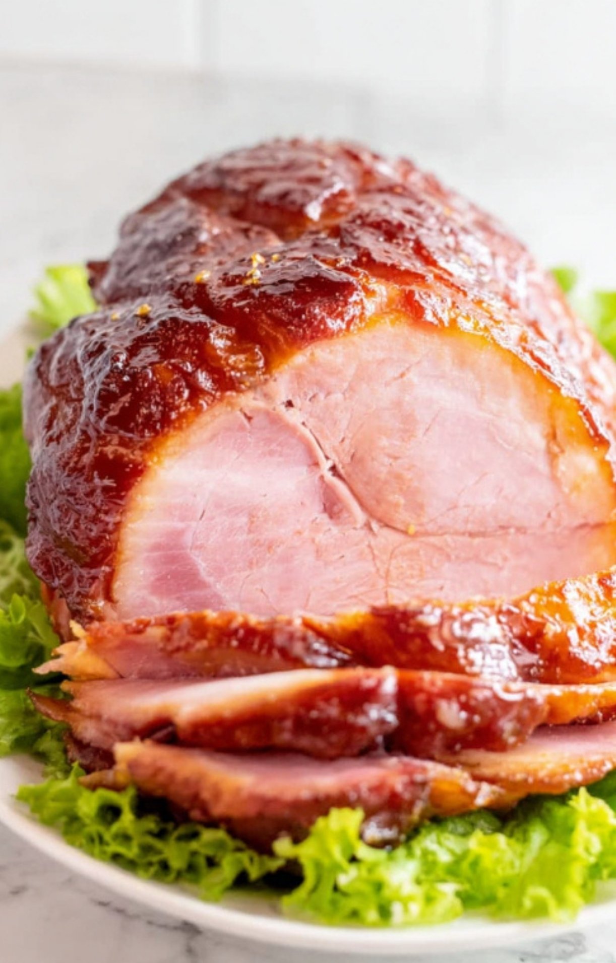 Double smoked ham on a platter with fresh lettuce, glossy glaze and thick slices, great for family dinner.