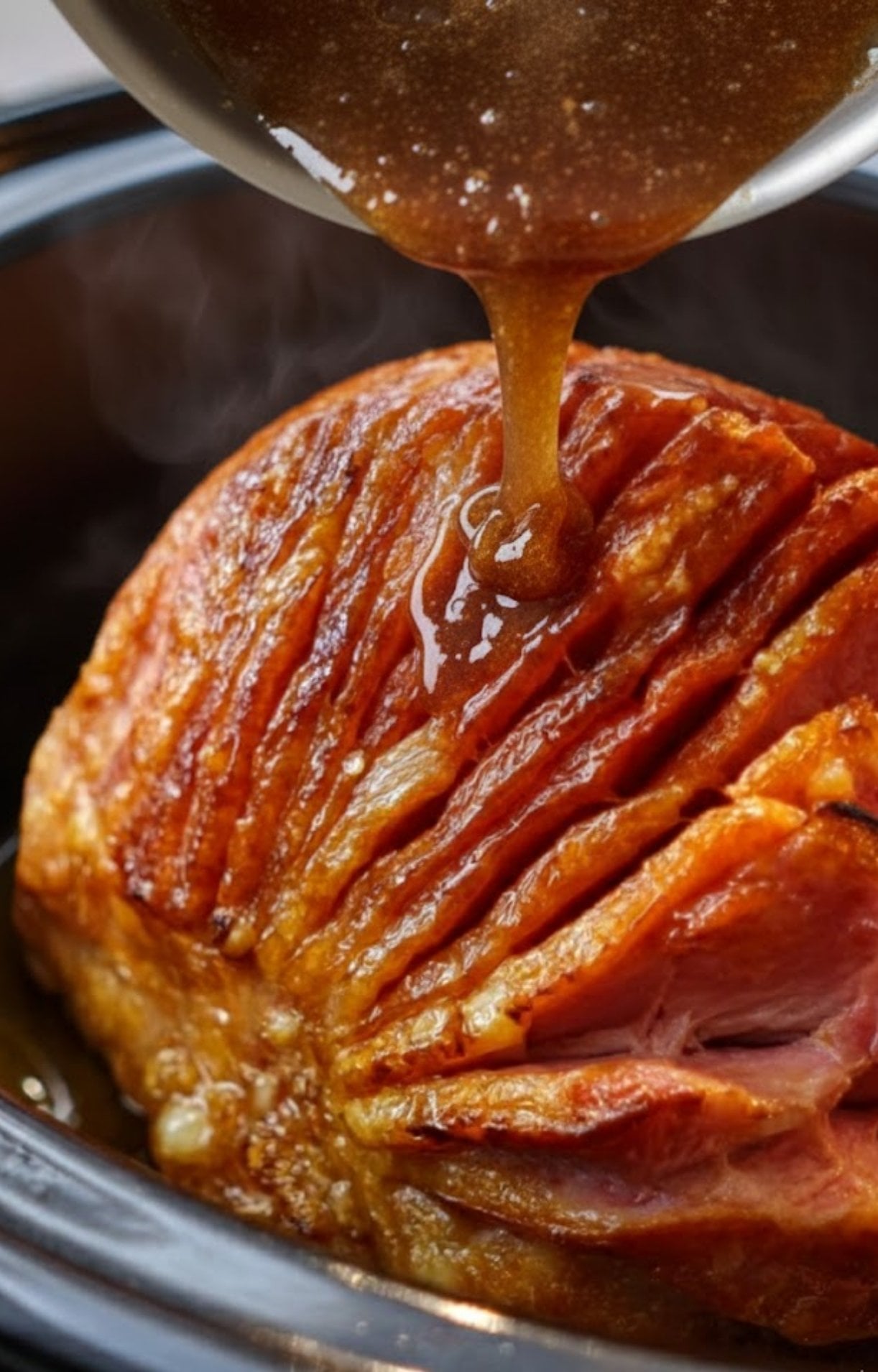 Thick brown sugar pineapple glaze poured from a saucepan onto a spiral ham in the crock pot.