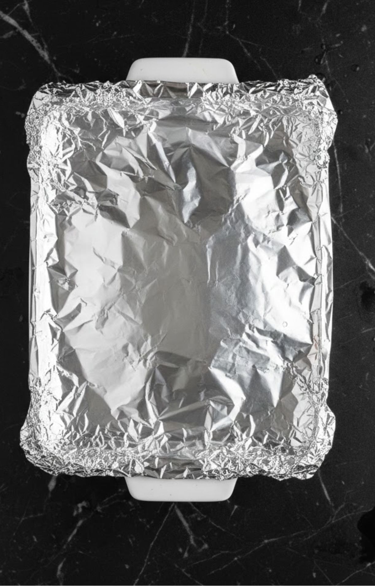 Baking dish tightly covered with aluminum foil, locking in moisture for oven reheating