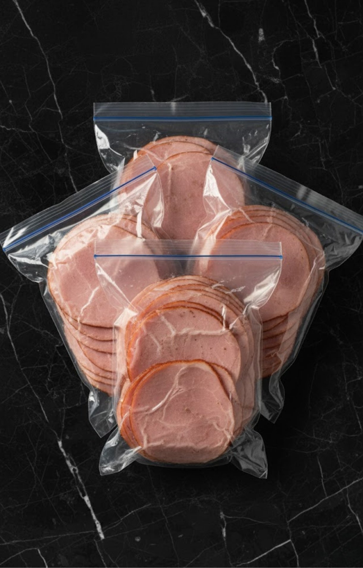 Several clear plastic airtight freezer bags filled with portions of sliced smoked ham to prevent freezer burn.