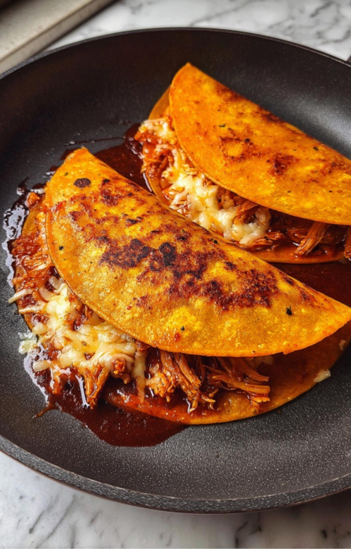 Two Chicken Birria Tacos folding over and frying in a pan until the cheese is melted and the edges are crispy.