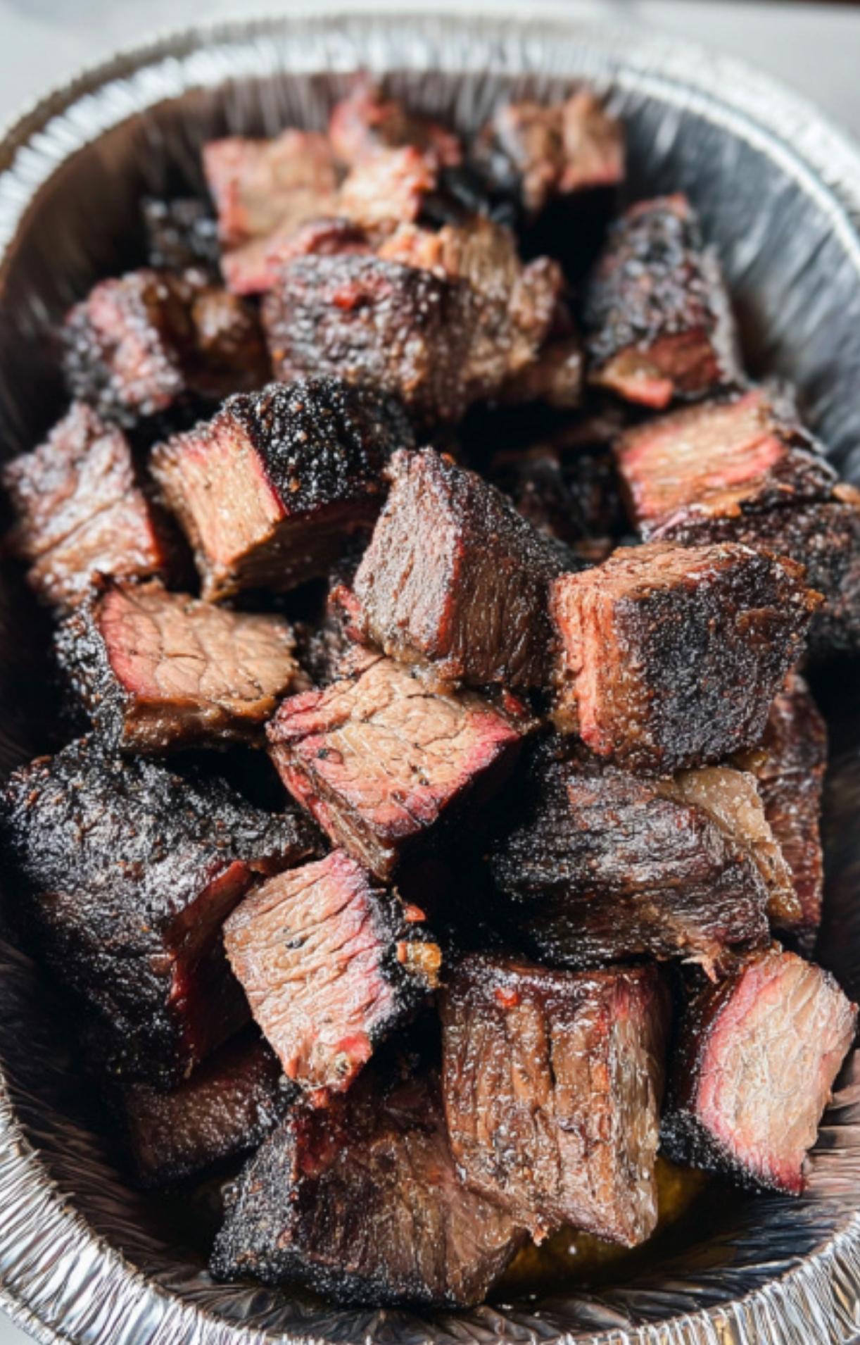 Smoked chuck roast cut into bite-sized cubes inside a disposable foil pan, revealing the pink smoke ring and juicy interior.
