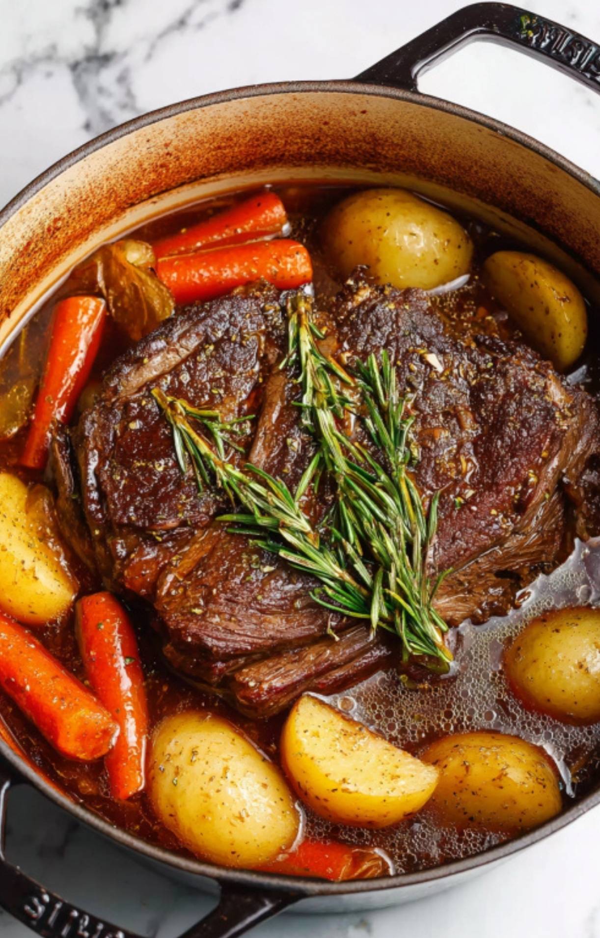 The Dutch oven filled with beef, vegetables, and fresh rosemary sprigs submerged in broth before cooking