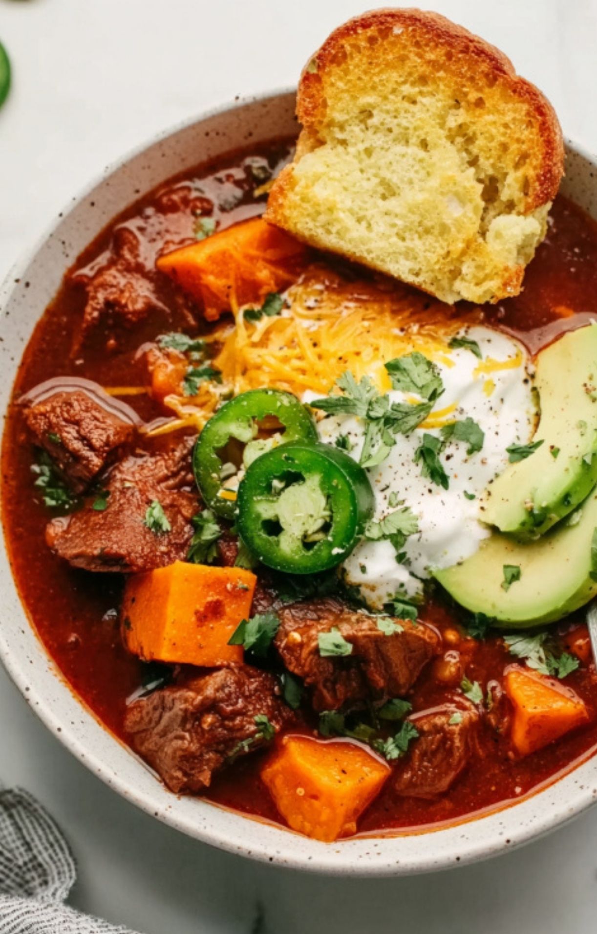A bowl of savory beef chili topped with melted cheese and sour cream, served with a side of golden toasted bread for dipping.