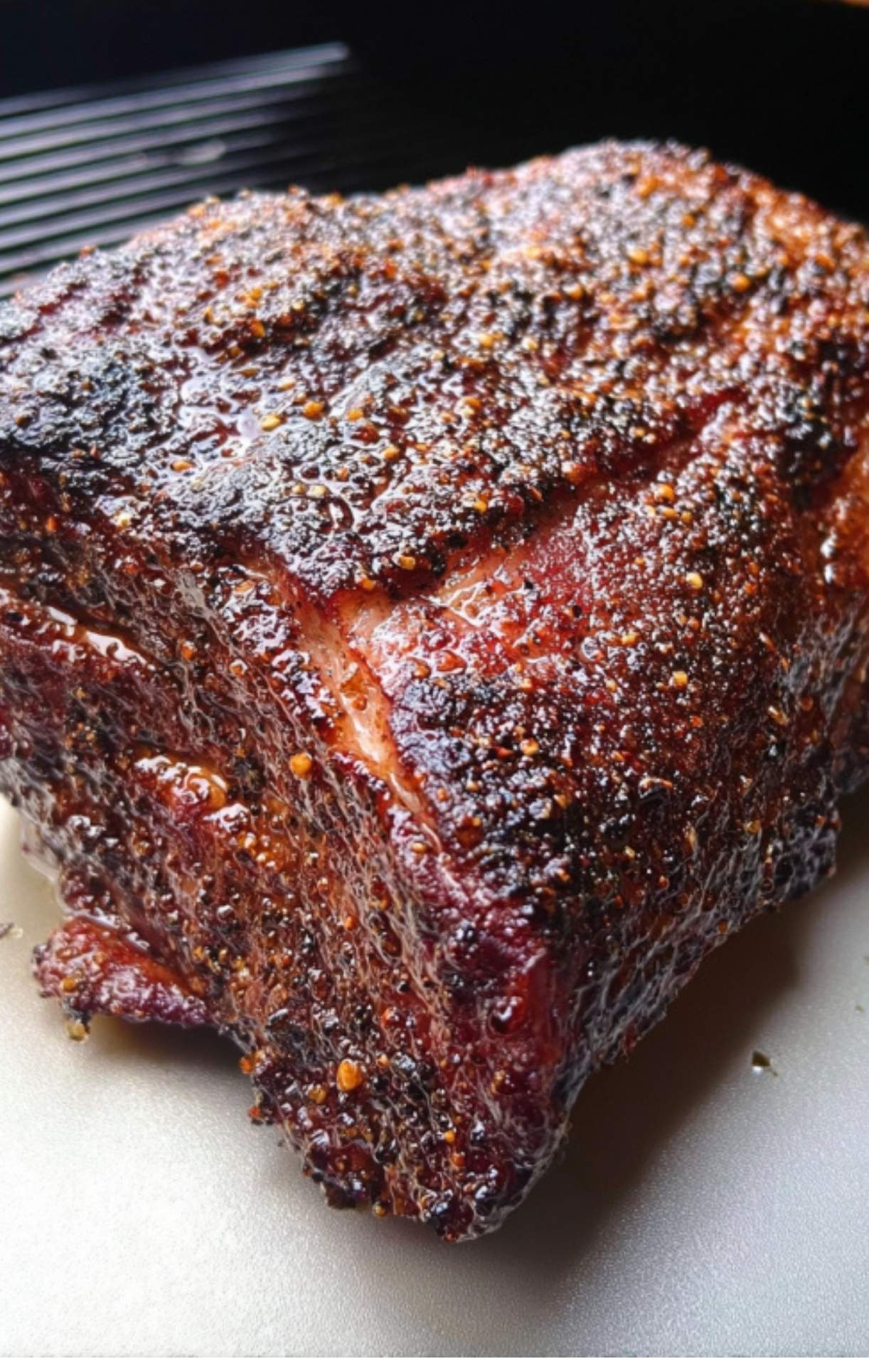 A close-up of a whole smoked chuck roast with a dark, glistening bark and visible peppercorns.