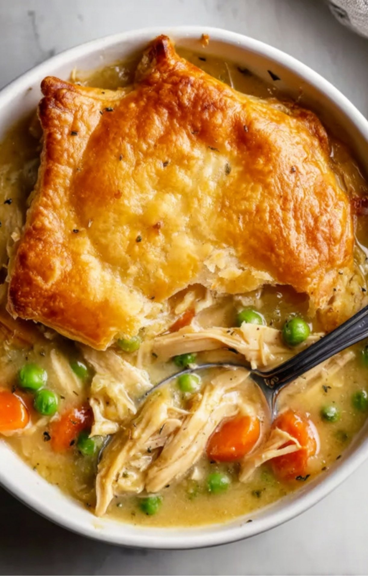 A top-down view of a single bowl of Gluten Free Turkey Pot Pie featuring a thick crust over shredded turkey, peas, and carrots.