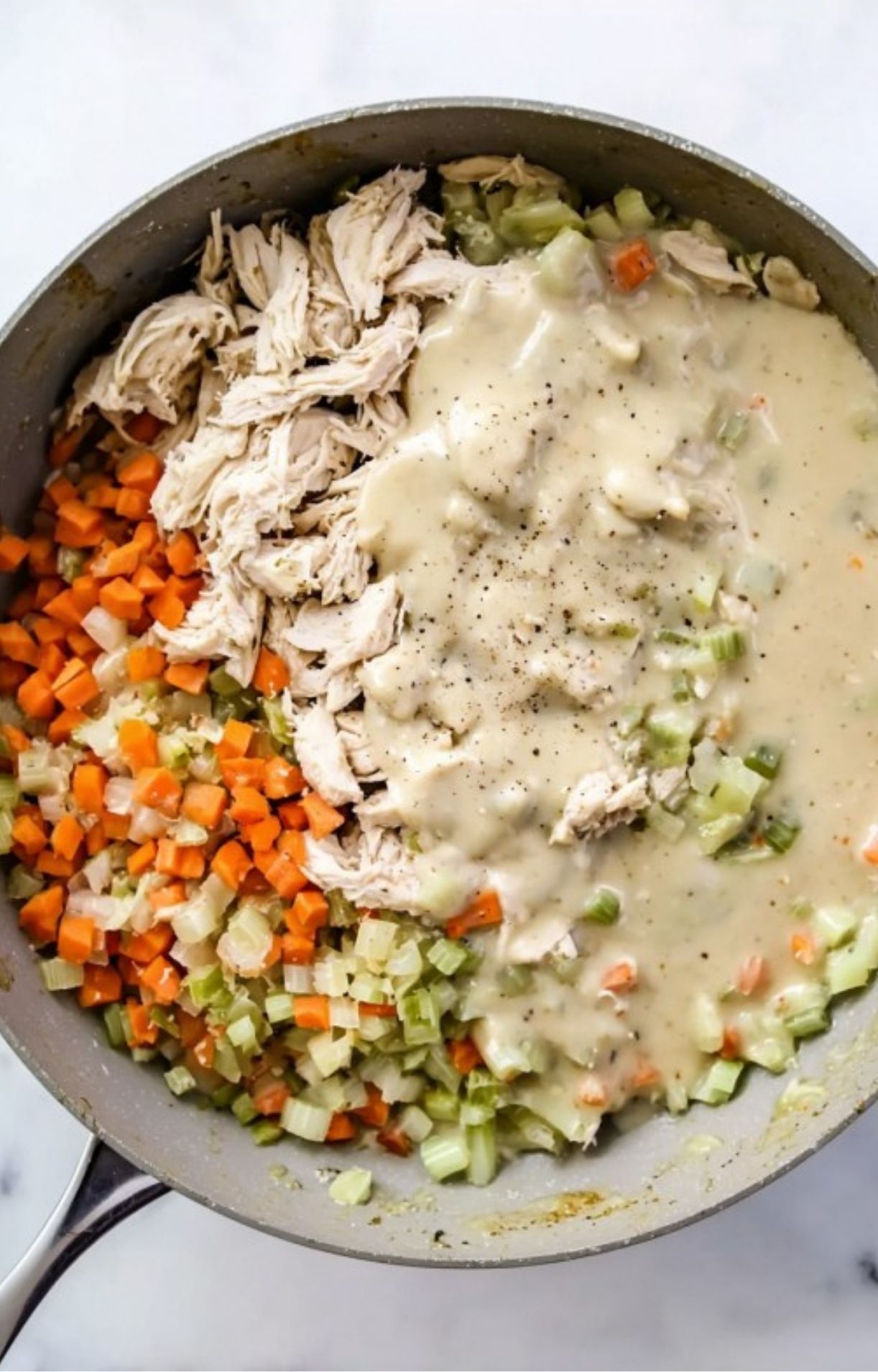 Shredded turkey and sautéed vegetables being mixed with a creamy white sauce in a large skillet to create the healthy turkey pot pie base.