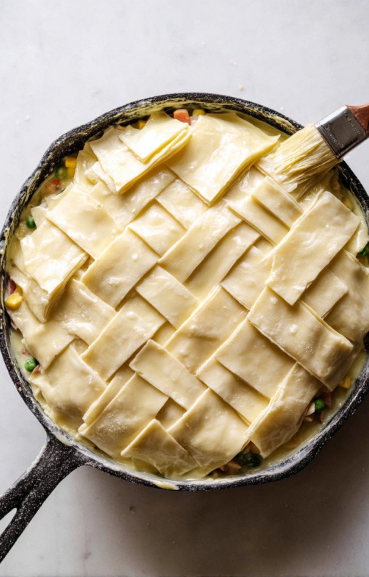 Strips of puff pastry being woven over the turkey filling and brushed with egg wash.