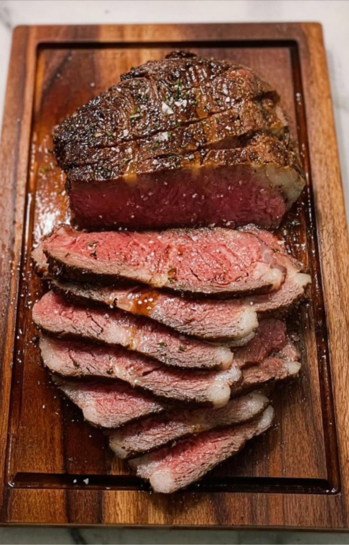 Perfectly cooked medium-rare ribeye steak sliced thin on a wooden cutting board and seasoned with sea salt.