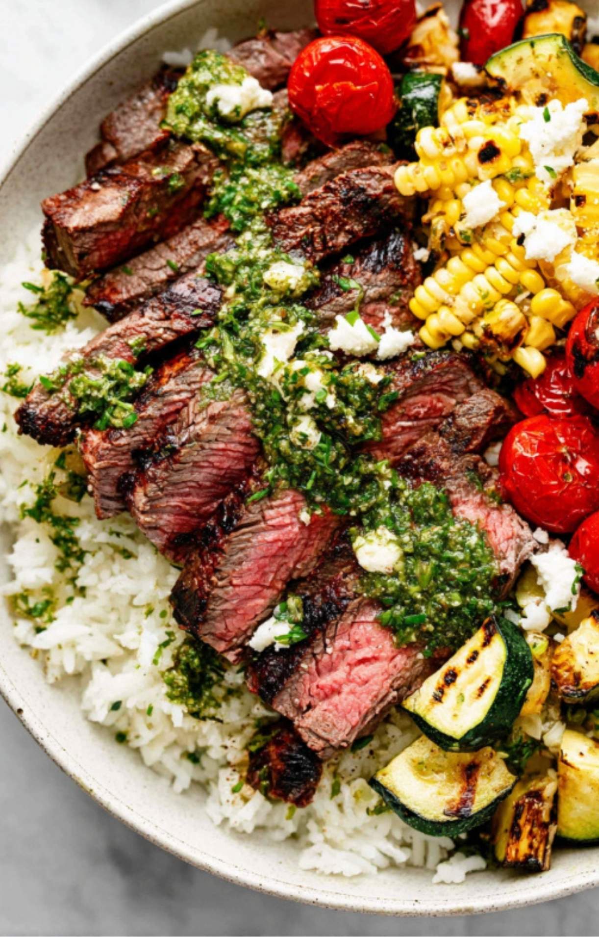 Sliced grilled steak topped with chimichurri sauce, served over white rice with roasted corn, zucchini, and cherry tomatoes