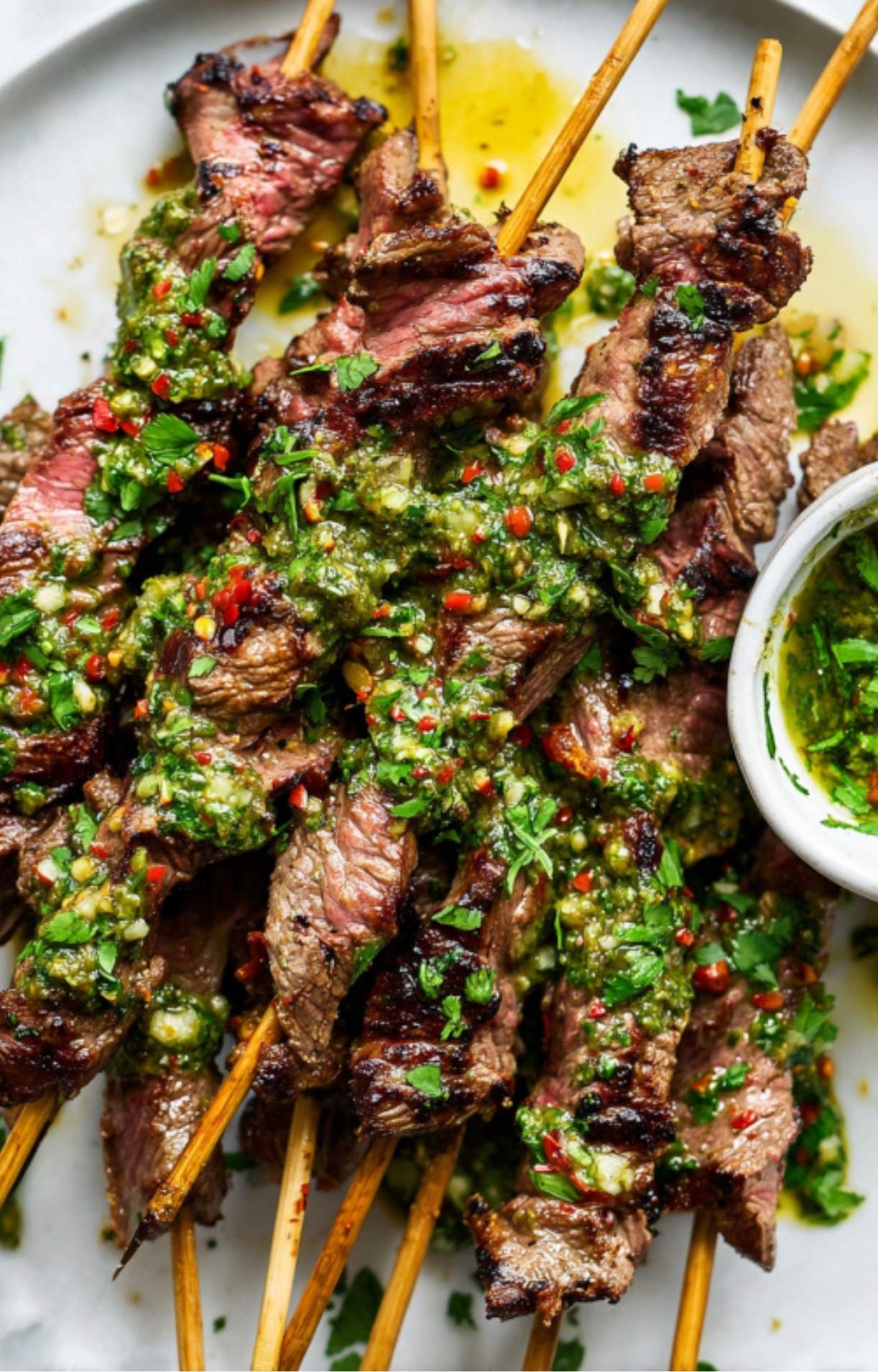 Juicy grilled steak skewers topped with green chimichurri sauce, served on a white plate.