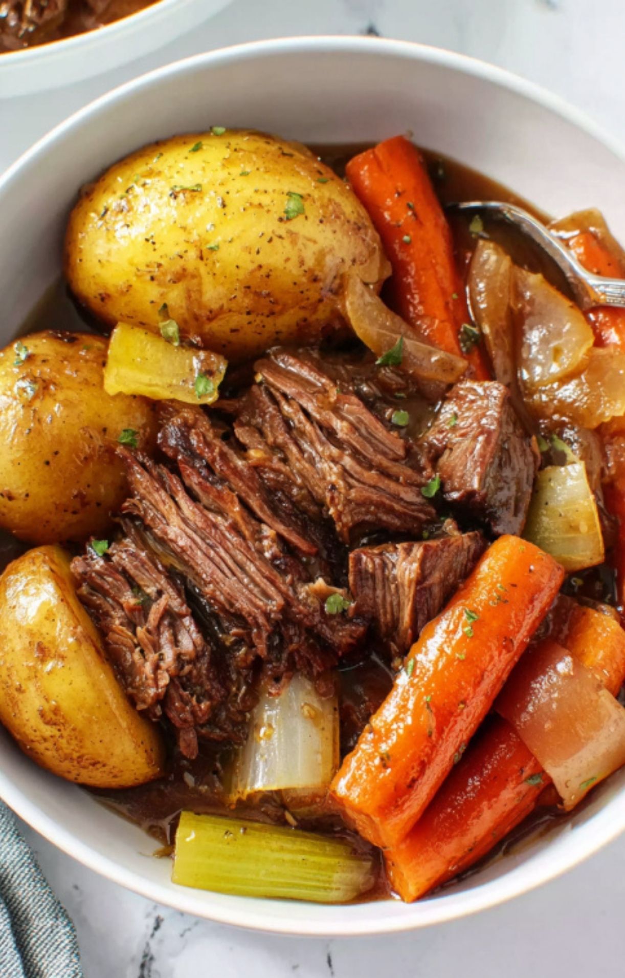 A close-up shot of a white bowl filled with shredded beef, a large golden potato, and tender cooked carrots