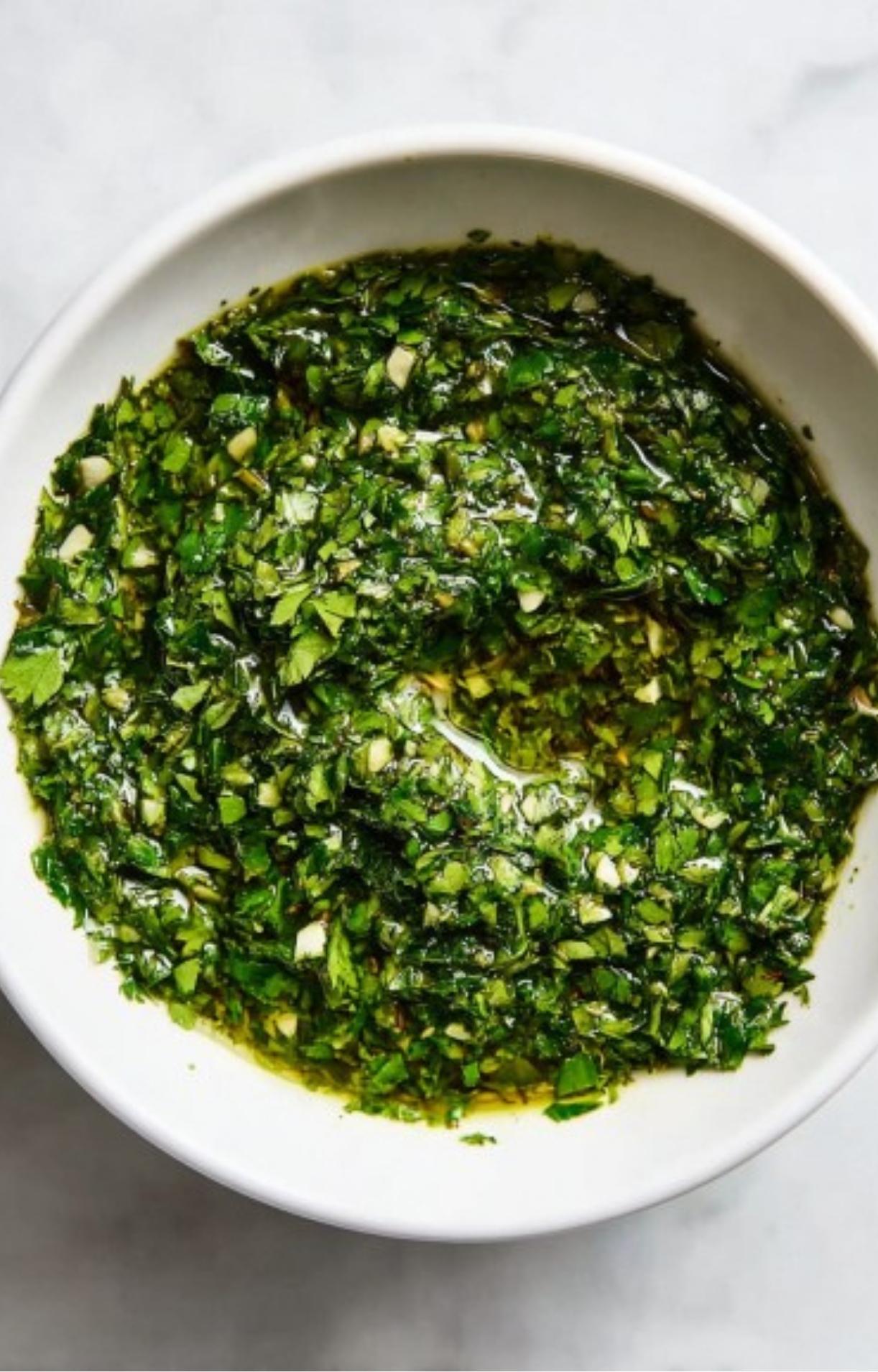 White bowl filled with homemade chimichurri sauce made from parsley, garlic, red pepper flakes, and olive oil.