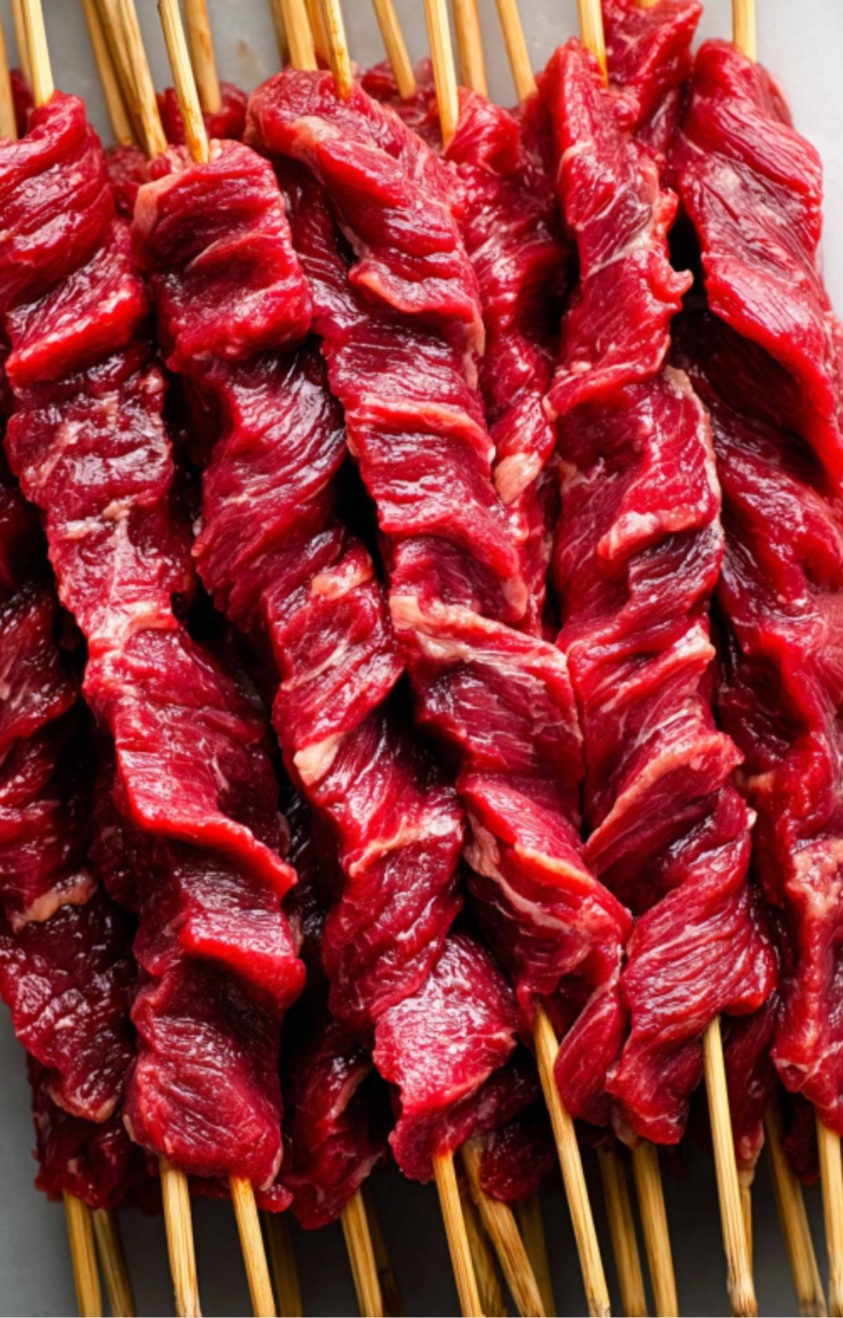 Uncooked beef strips twisted onto wooden skewers, ready to go on the grill.