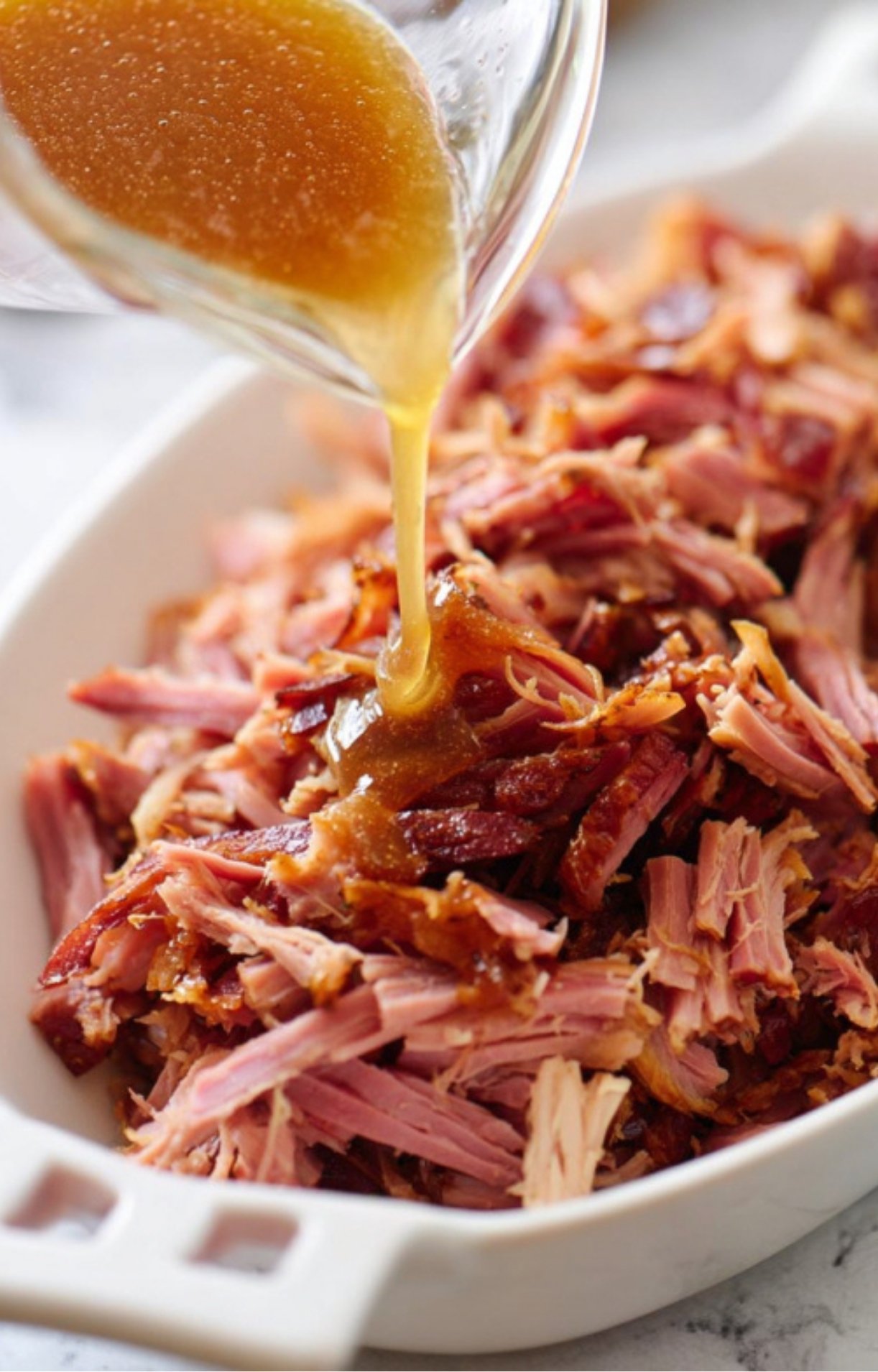 Sweet citrus glaze poured over hot pulled ham in a serving dish