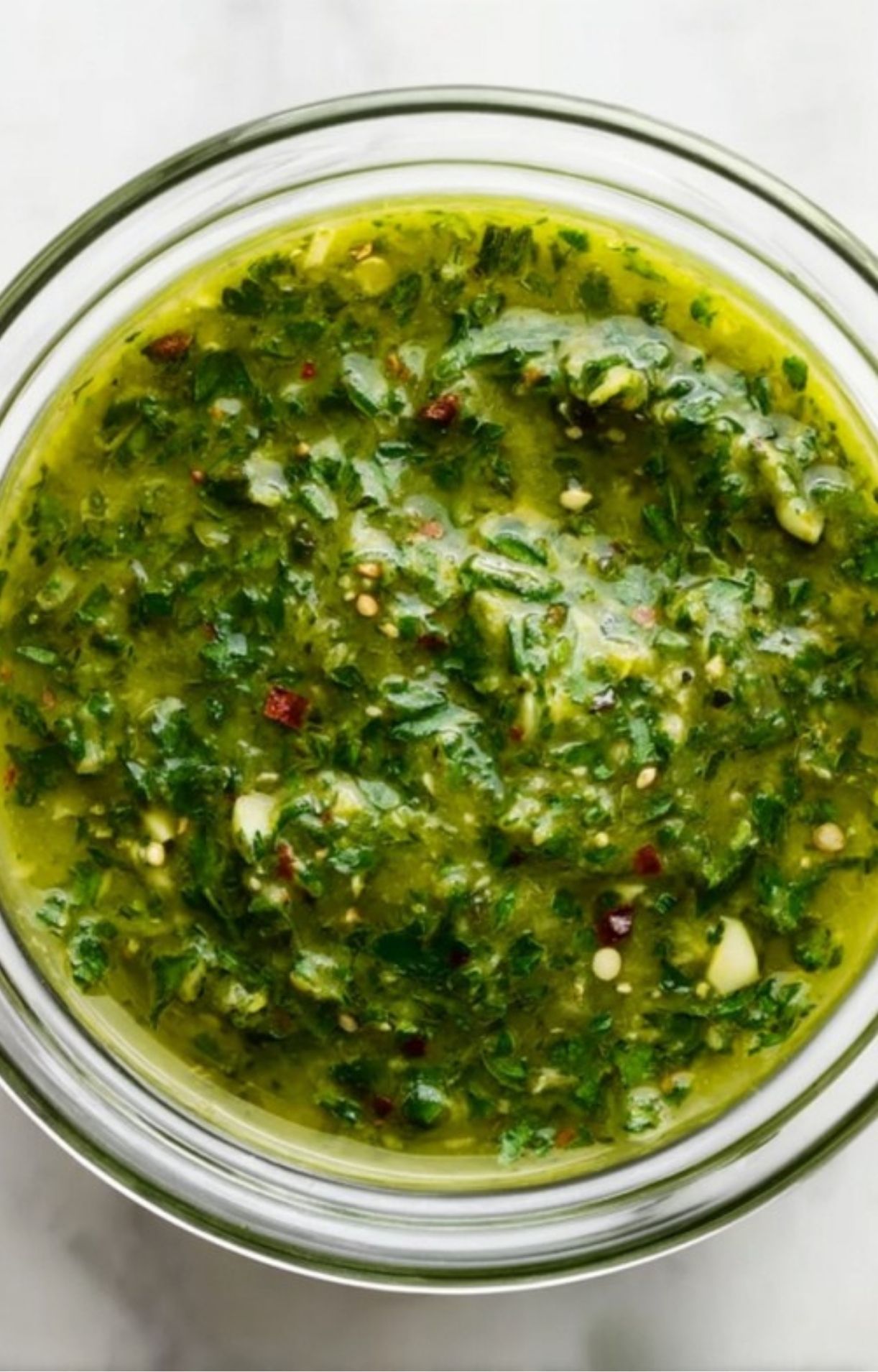Glass bowl filled with bright green chimichurri sauce made with herbs, garlic, and olive oil.
