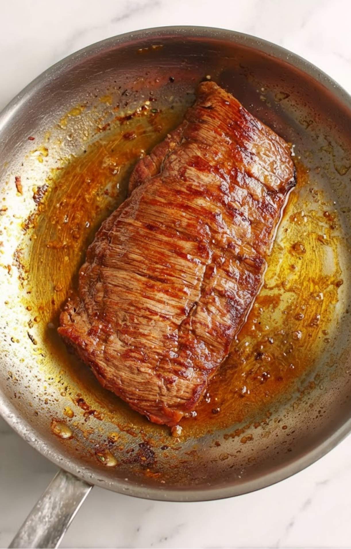 Juicy steak cooking in a stainless steel skillet, browning in oil, as part of the taco preparation.