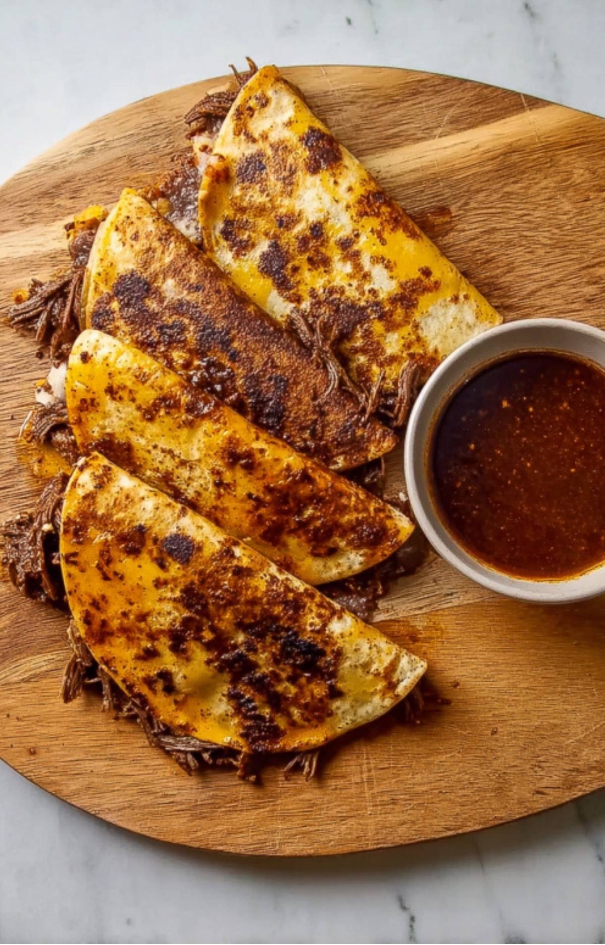 Four crispy, oil-stained folded tacos stuffed with shredded beef and melted cheese, served with a side of dipping consommé.