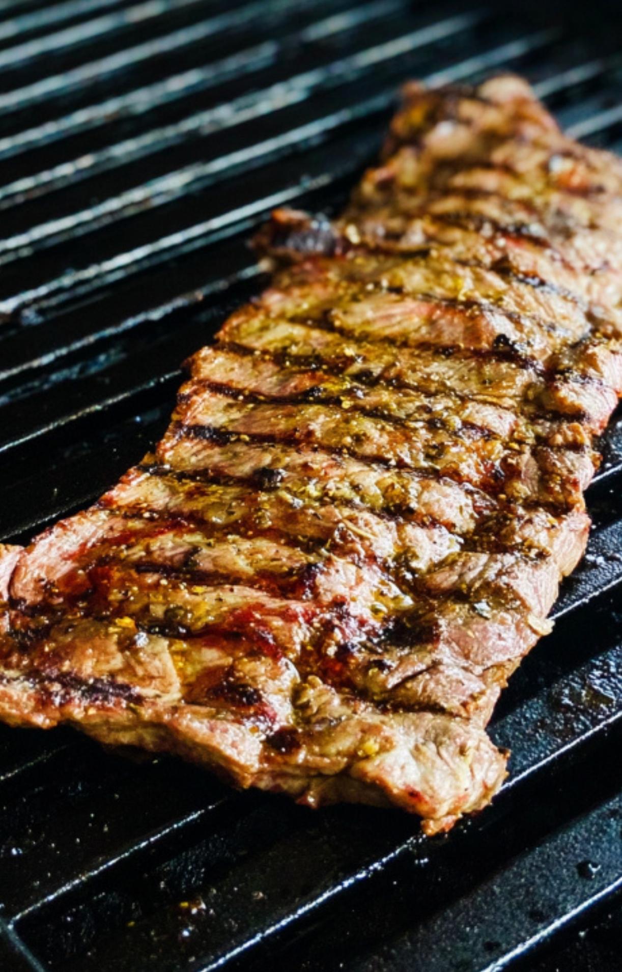 Skirt steak sizzling on a hot grill with visible sear marks, showing the perfect grilling process for juicy and tender results.