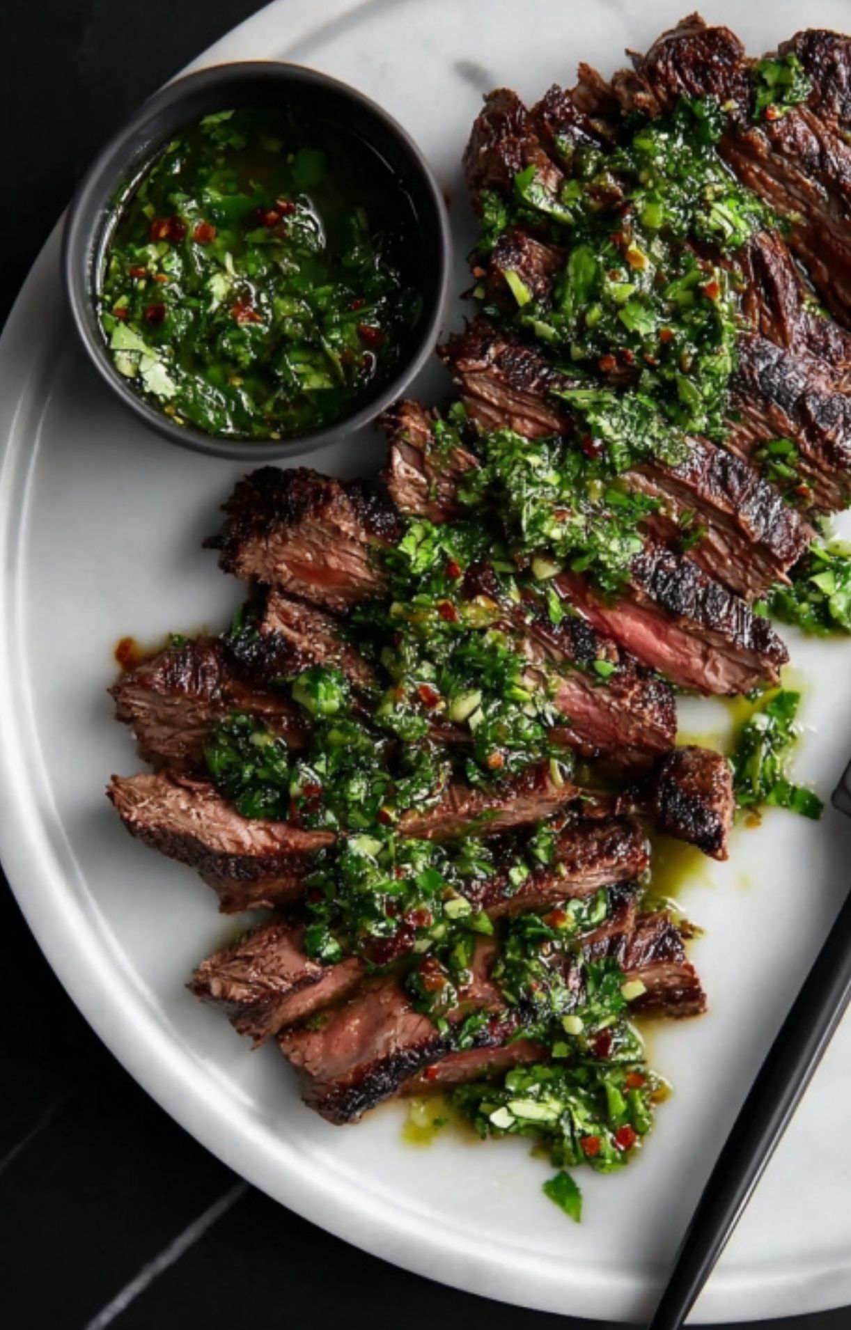 Platter of sliced skirt steak covered in homemade chimichurri, with extra sauce on the side. Ideal for entertaining, healthy dinners, and summer BBQ.