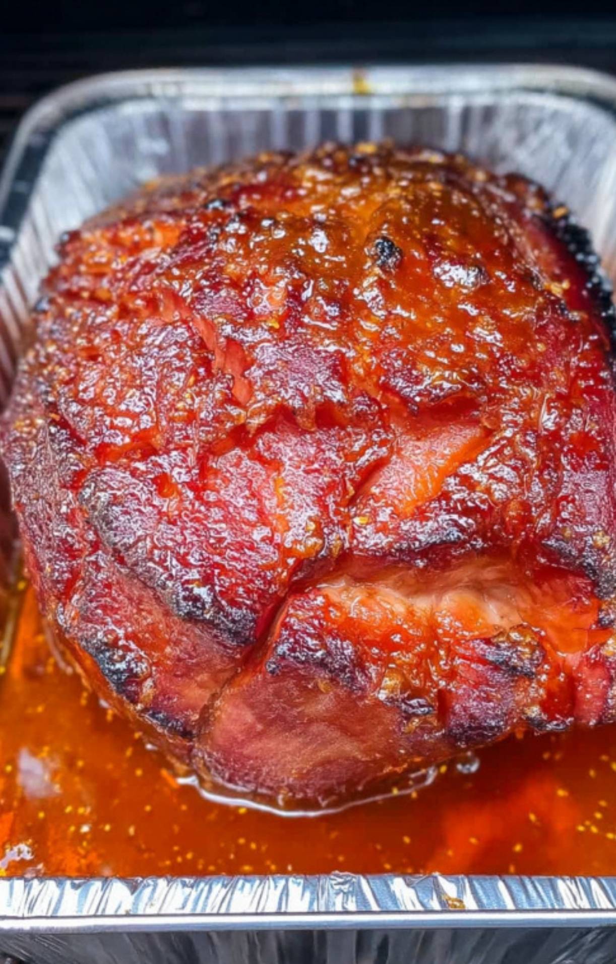 Double smoked ham in a foil pan on the grill, covered in sticky maple glaze, ready for smoking.
