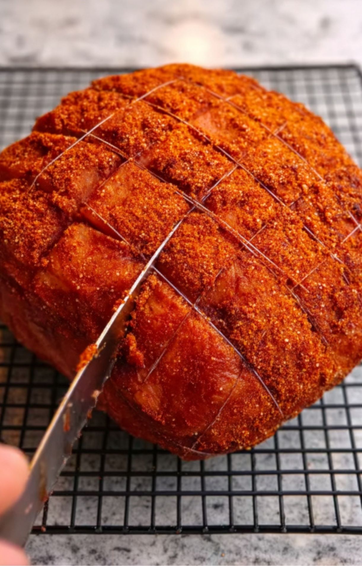 Scoring fresh ham coated in dry rub before smoking