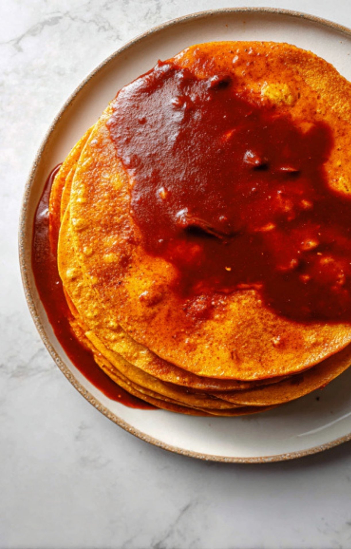 A stack of corn tortillas being dipped into the oily, flavorful red birria consomé.