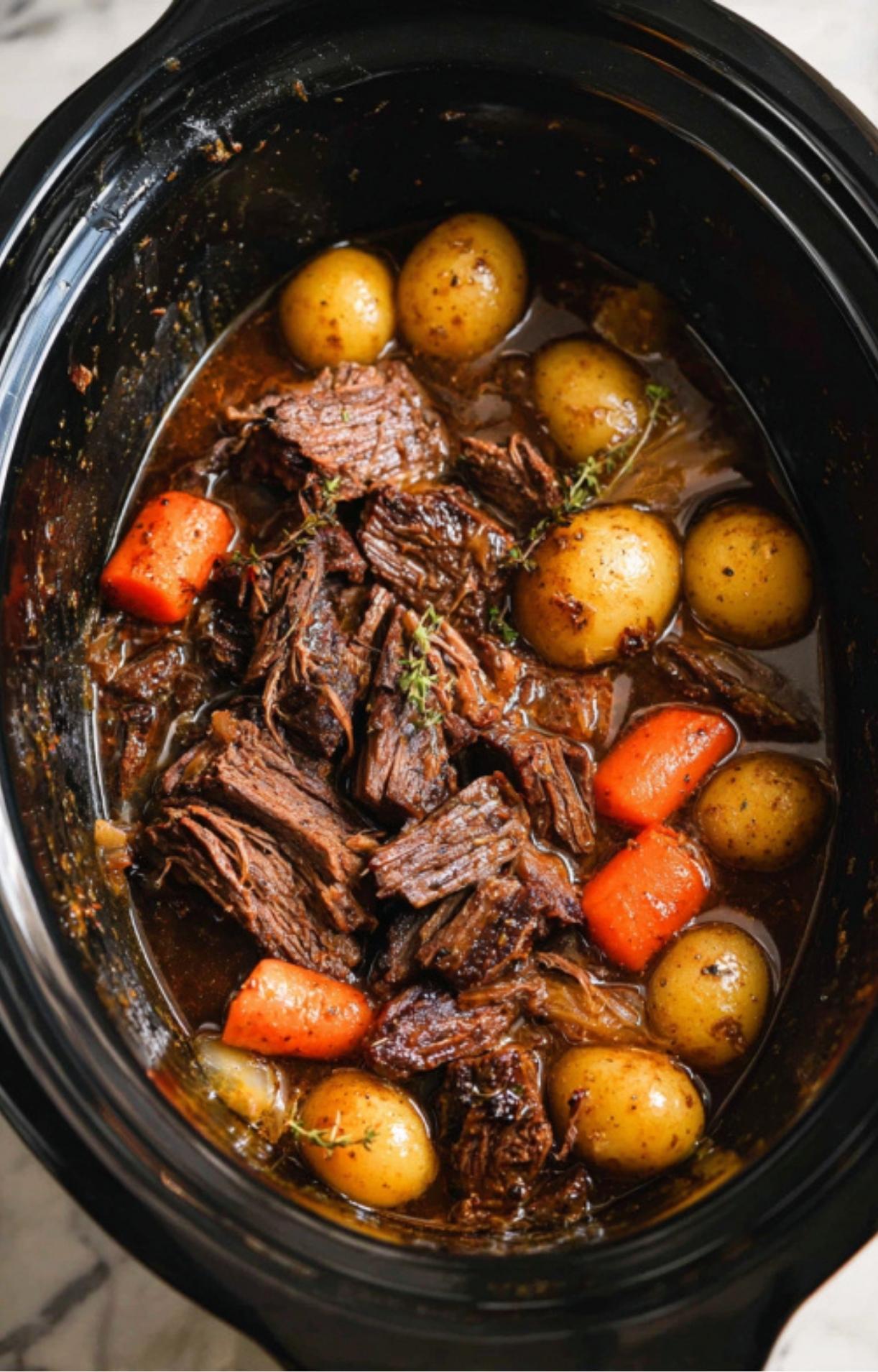 A large, raw beef chuck roast placed on top of the bed of potatoes, carrots, and onions in the slow cooker.