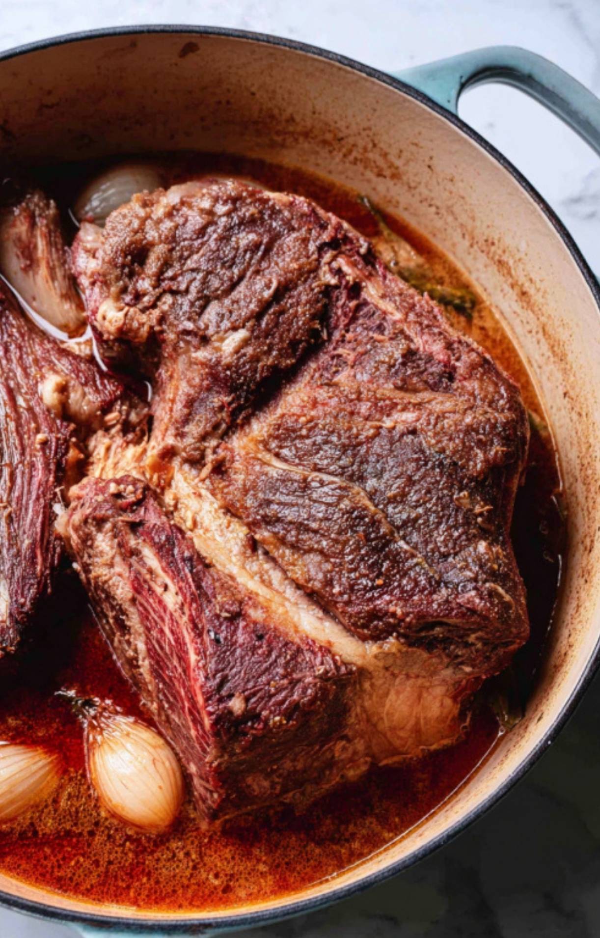 The seared roast submerged halfway in a rich broth with shallots, ready for a slow cook.