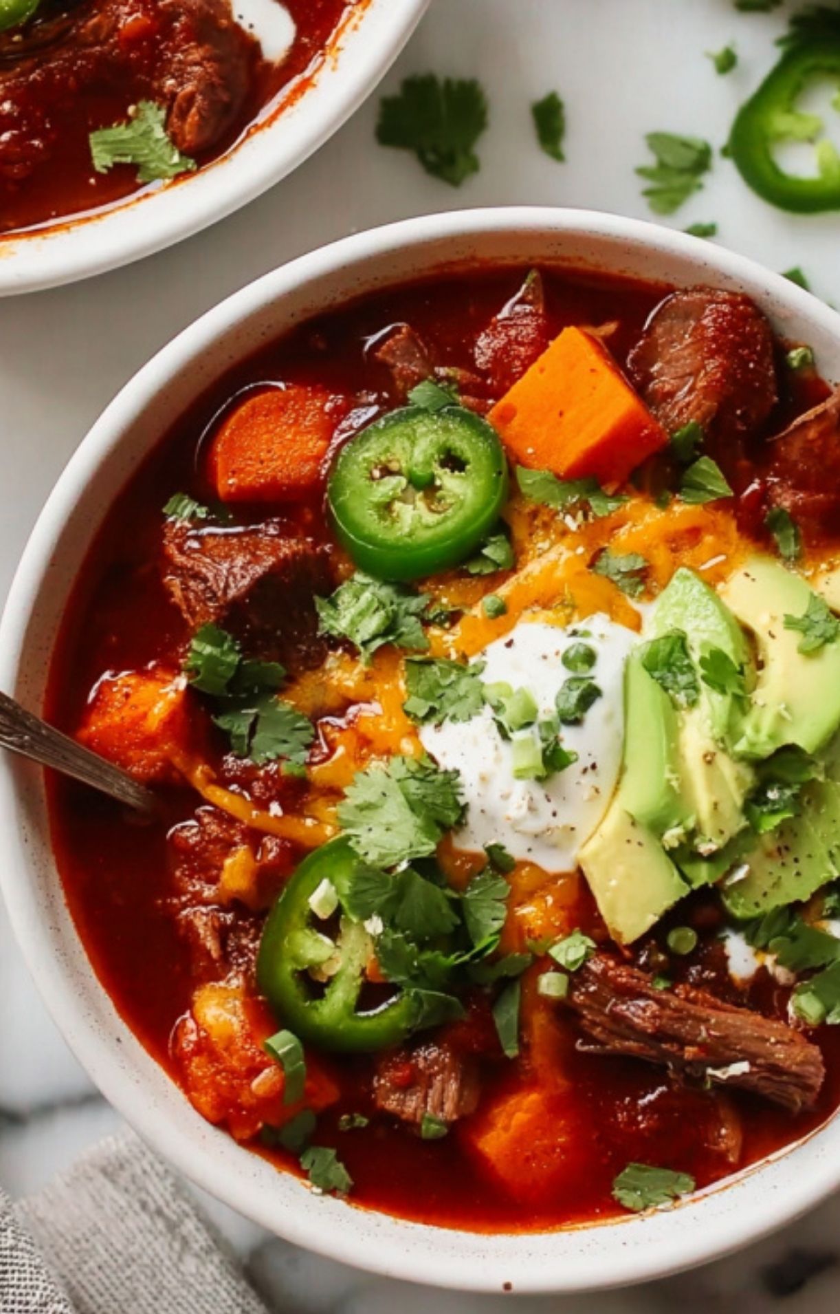 An overhead close-up shot of a bowl of chili showcasing the vibrant colors of fresh cilantro, jalapeño rings, and creamy avocado toppings.