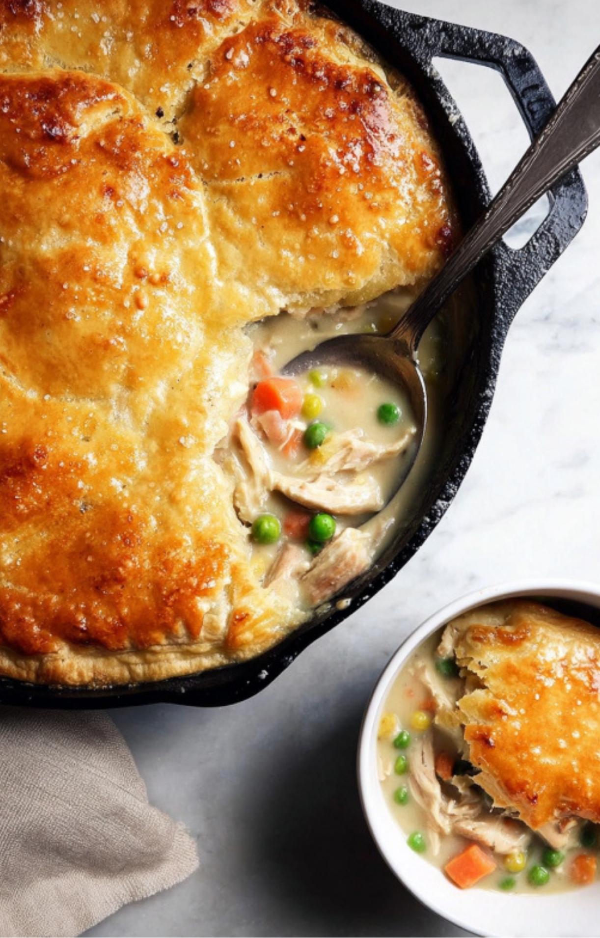 A large spoon scooping out a portion of Gluten Free Turkey Pot Pie from a cast-iron skillet into a white ceramic bowl.