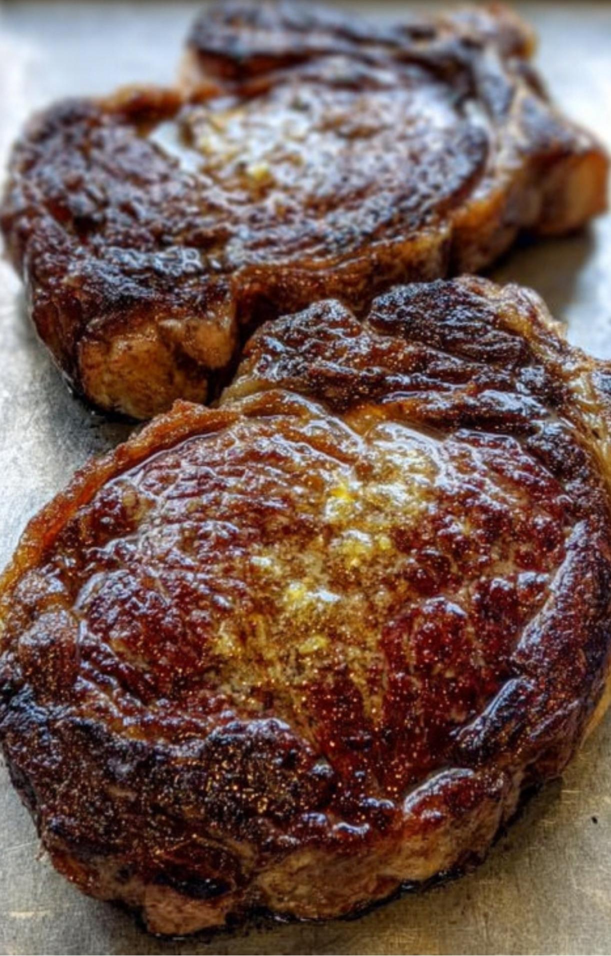 Two rib eye steaks on a baking sheet showing a perfectly browned, caramelized crust before entering the oven.