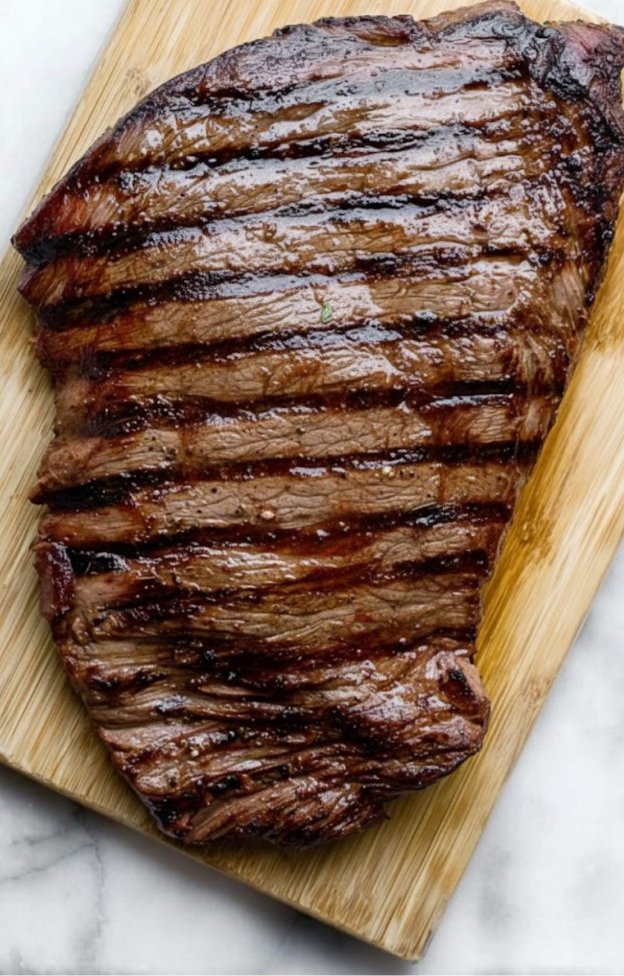 Perfectly grilled flank steak resting on a wooden cutting board, ready to be sliced.