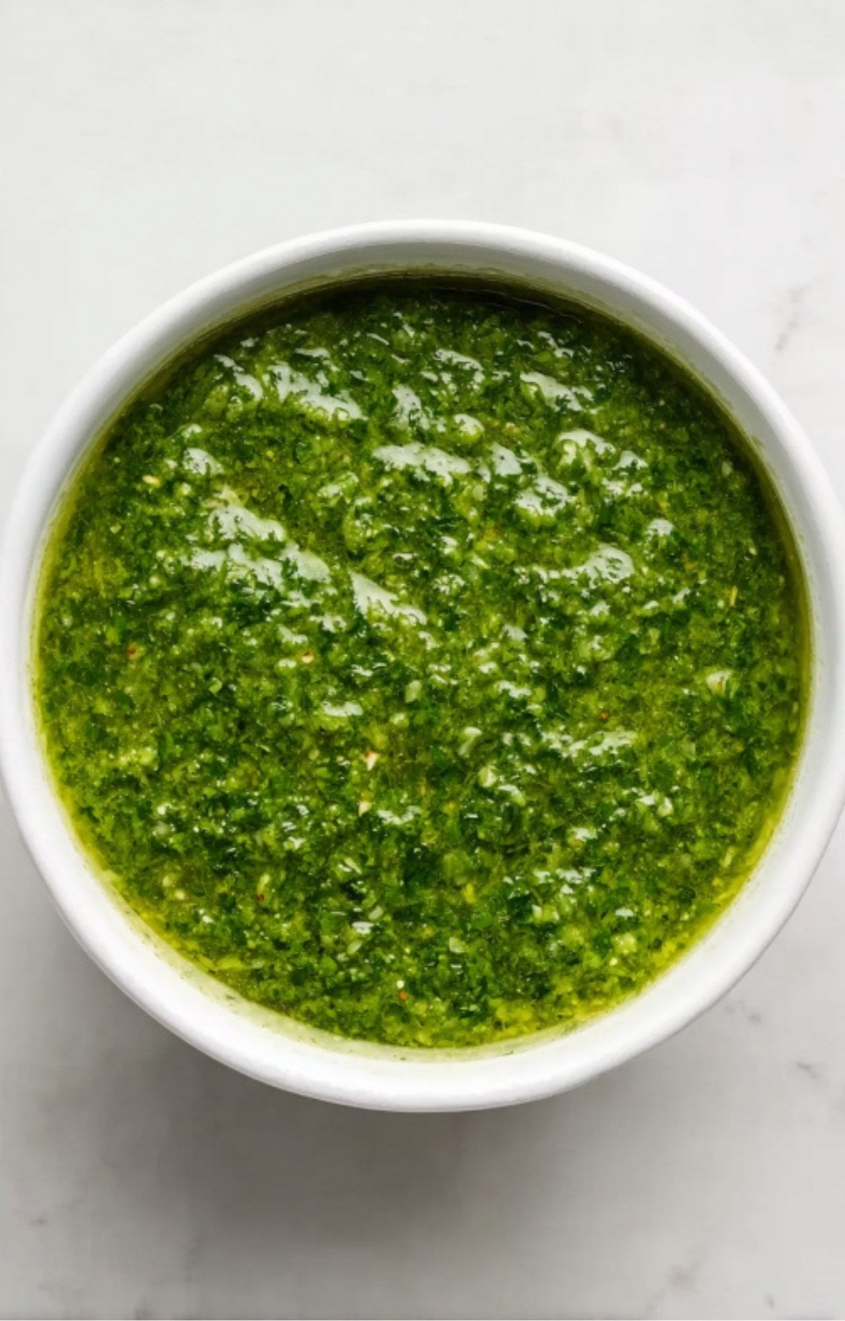 Bright green chimichurri sauce made with fresh parsley, garlic, olive oil, and vinegar in a white bowl.
