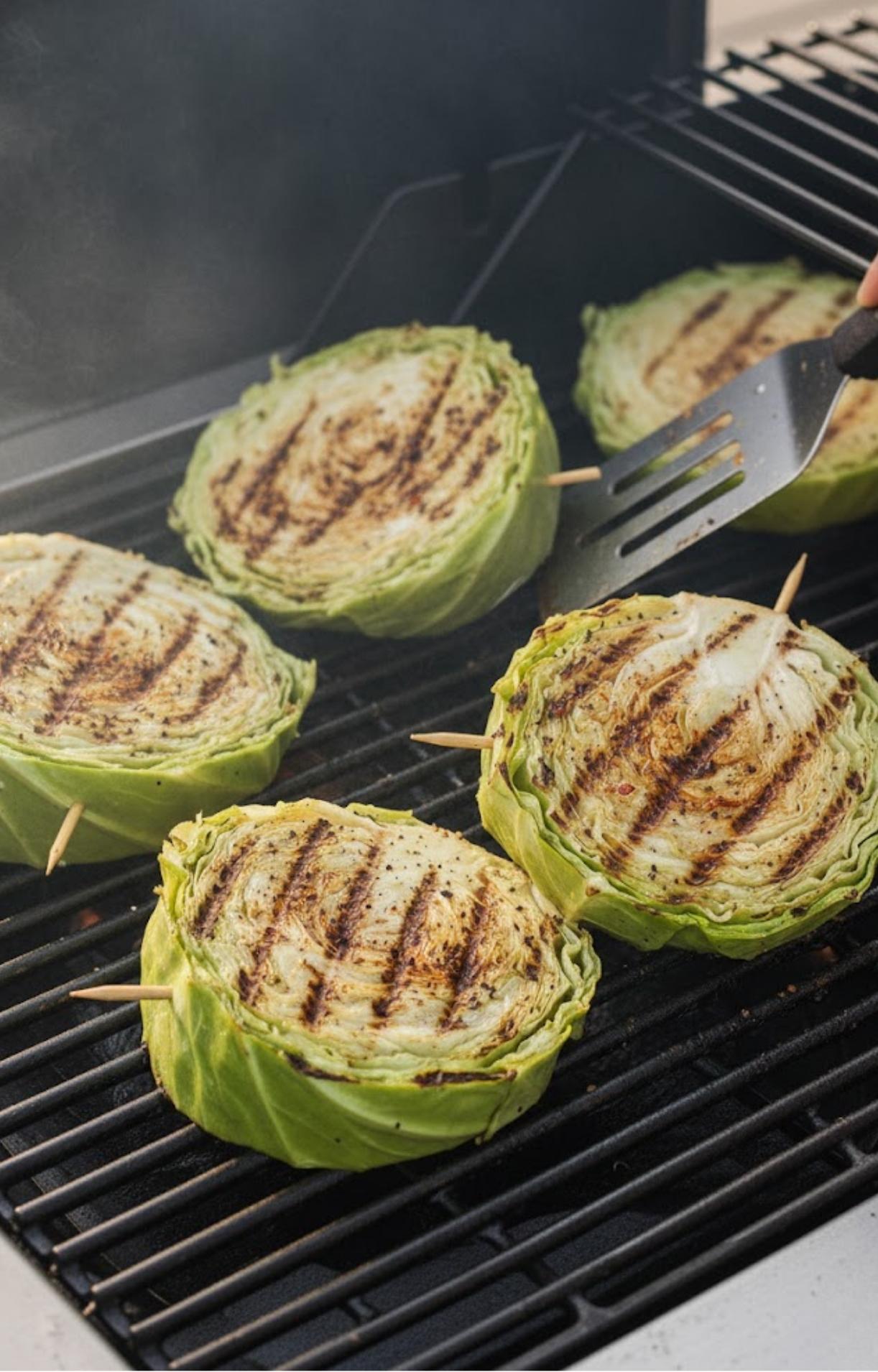 Thick slices of cabbage grilling on a barbecue with visible char marks, held together by wooden skewers.