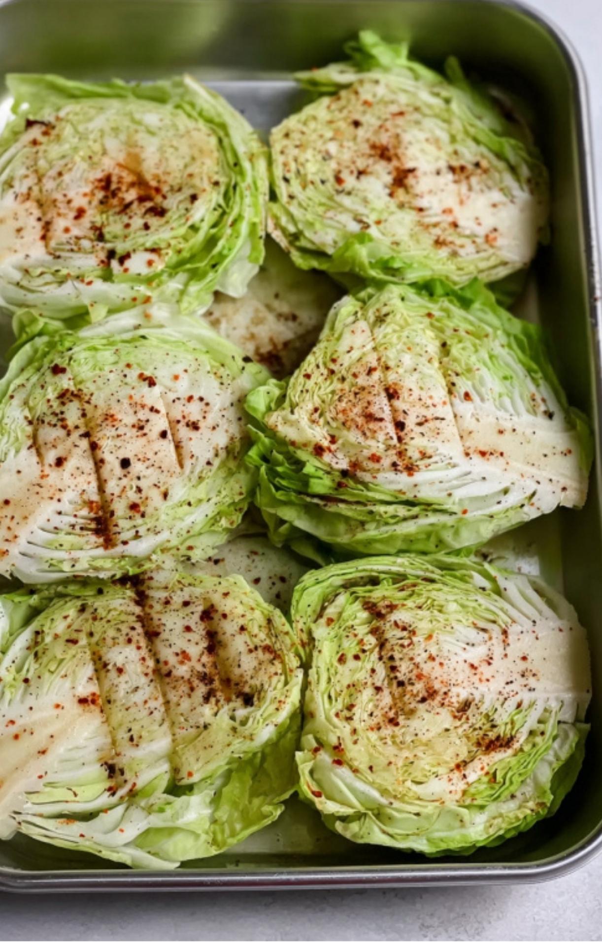 Thick slices of cabbage in a pan, seasoned and ready to be grilled.