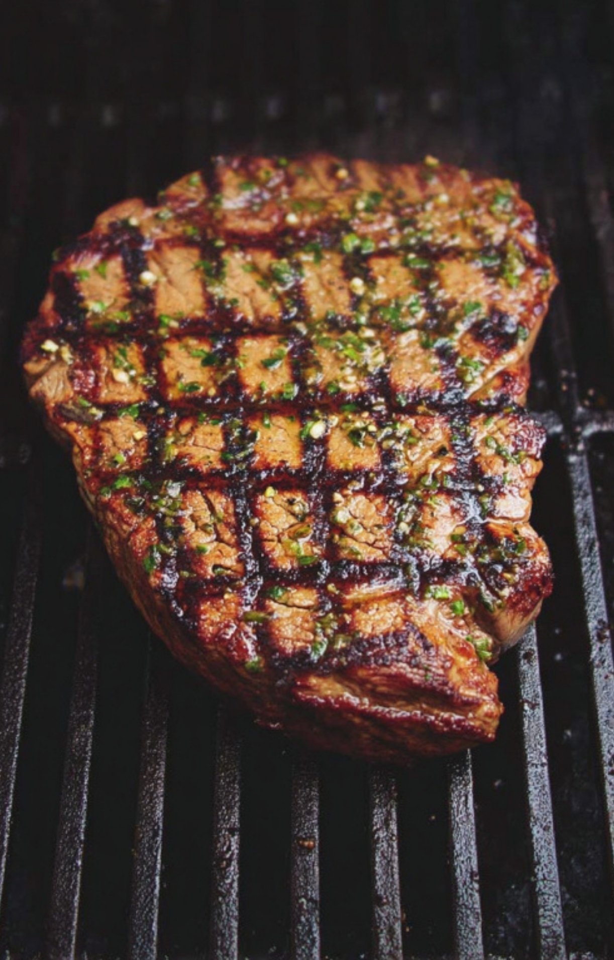 Juicy steak sizzling on a hot grill, topped with fresh chimichurri sauce.