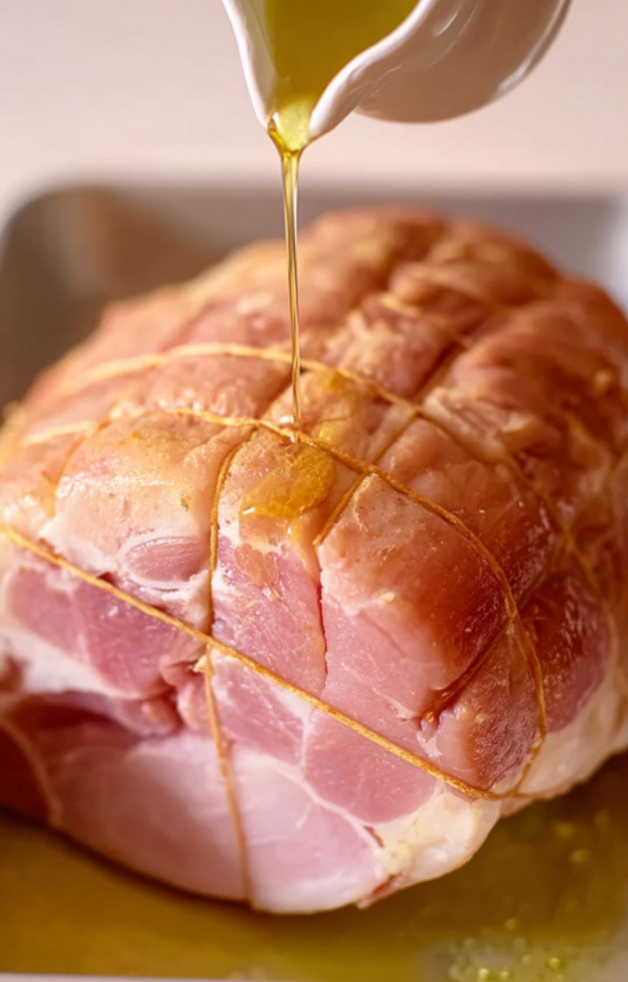Olive oil being poured over an uncooked ham roast with butcher’s twine, getting ready for the smoker.