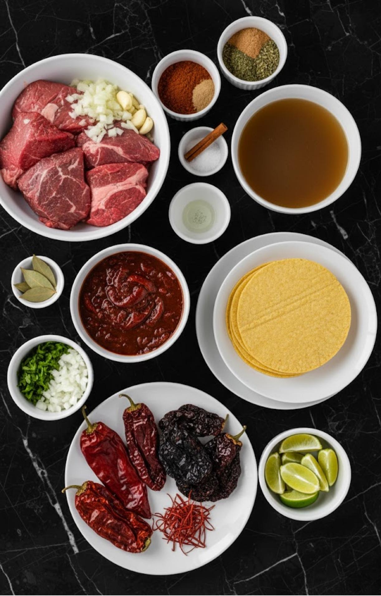 An overhead shot of ingredients for Crockpot Birria Tacos, including beef chunks, dried chilies, spices, beef broth, and corn tortillas.
