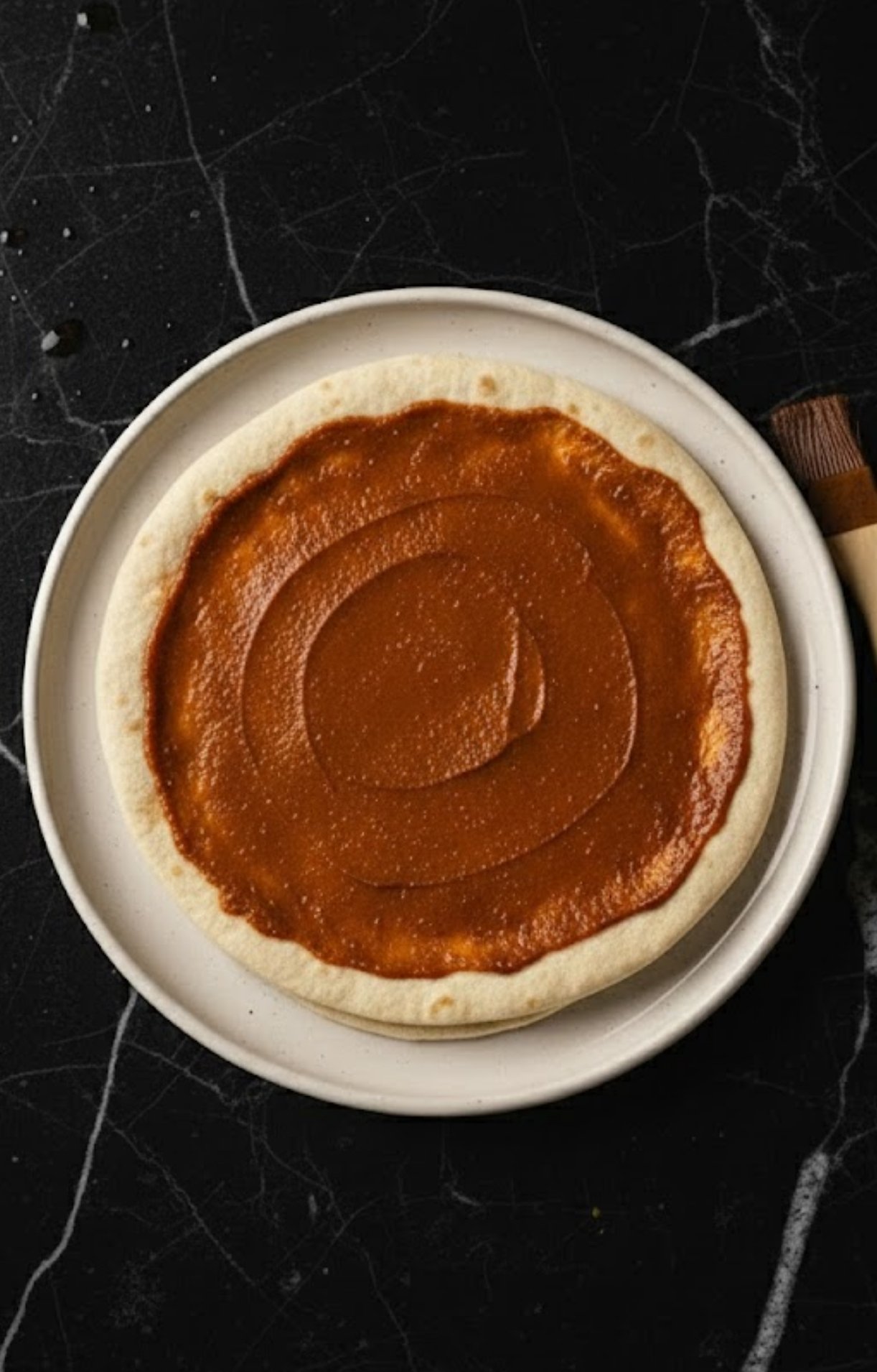 A smooth, even layer of red birria-style sauce spread across the center of the dough.