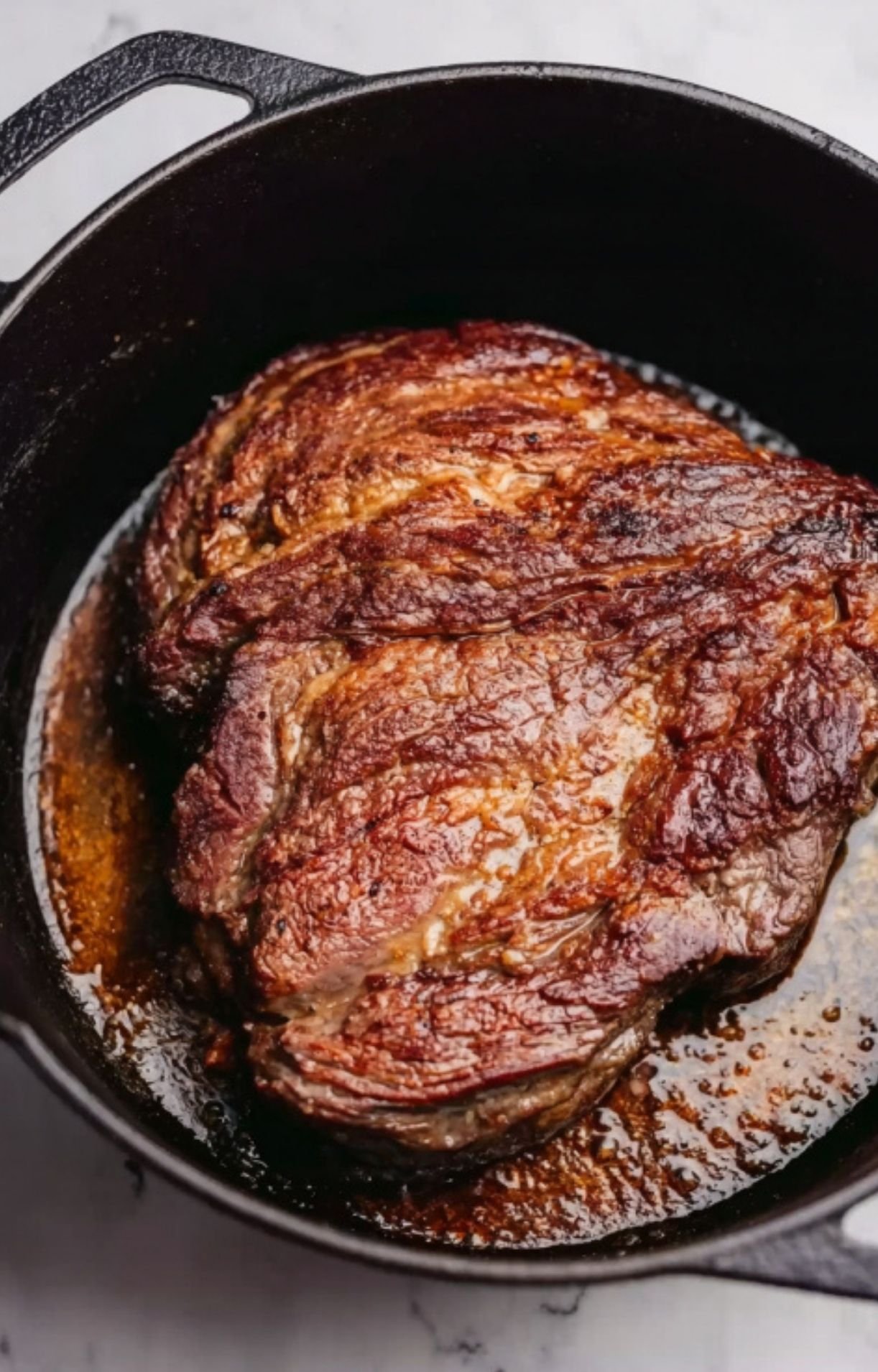 A beef chuck roast being browned in a black cast iron Dutch oven until a dark crust forms.