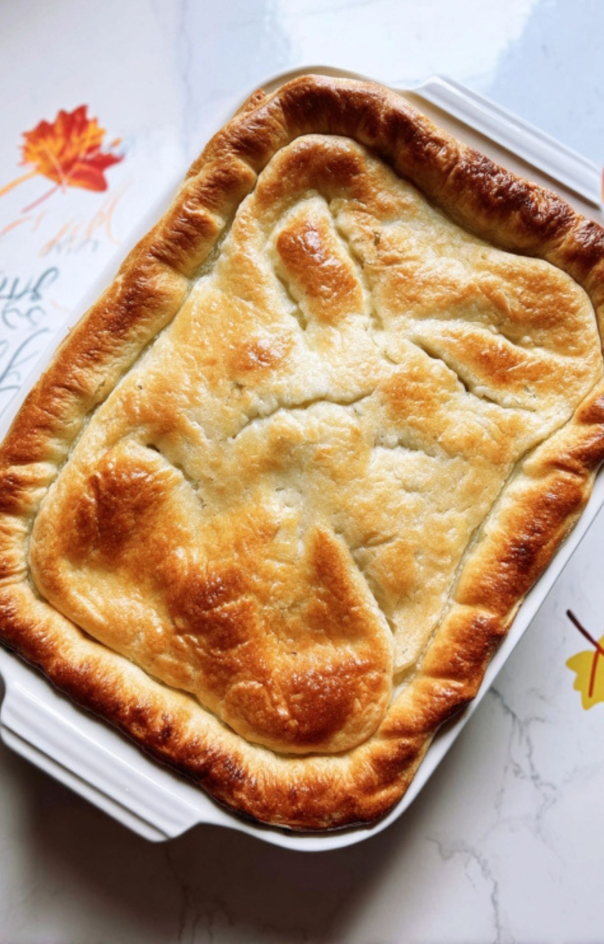 A top-down view of the Turkey Pot Pie with Crescent Rolls in a white baking dish, featuring a perfectly browned and flaky golden crust.