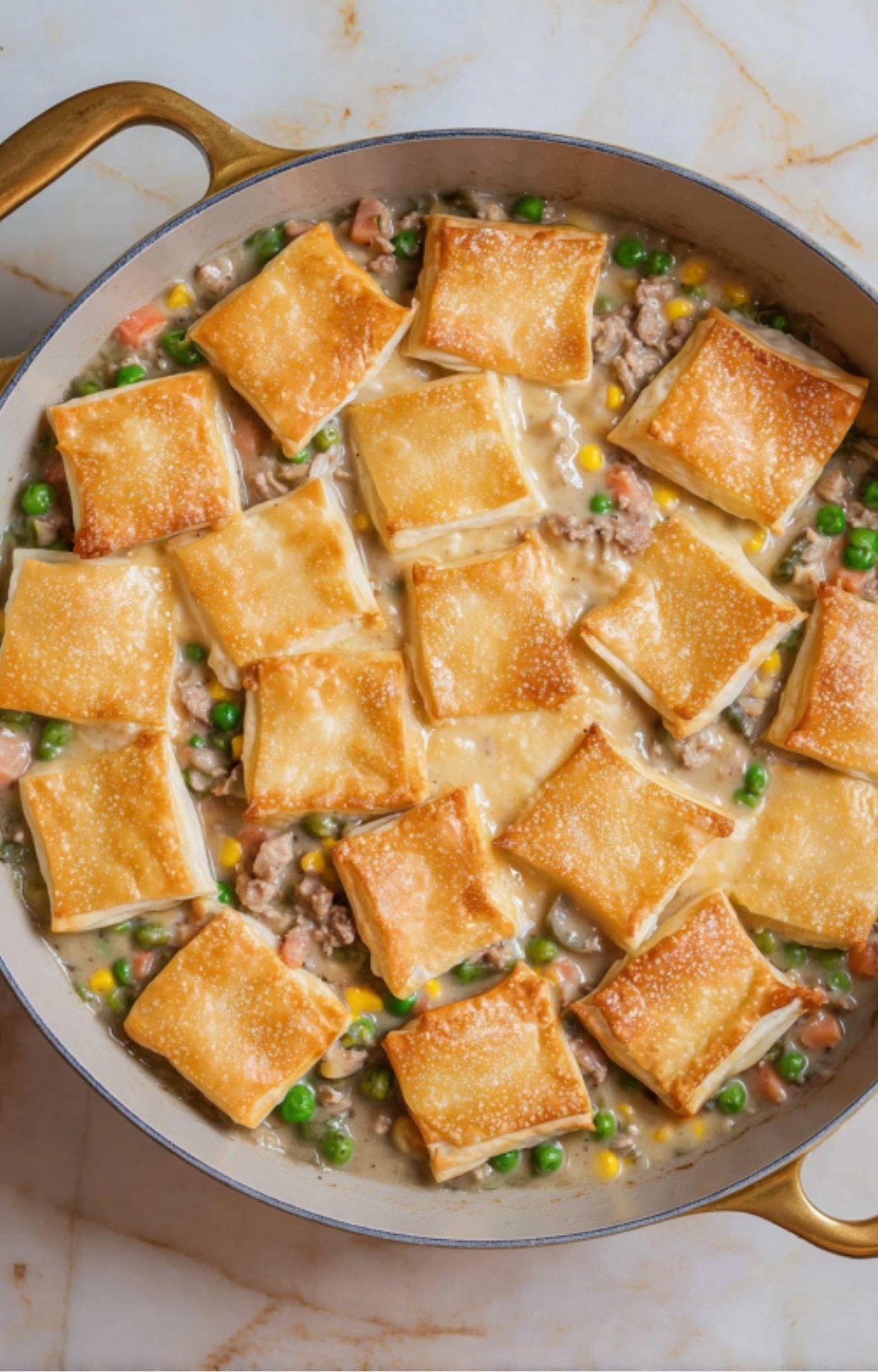 Rectangular pieces of raw puff pastry being arranged in a decorative pattern over the turkey and vegetable filling in the skillet.