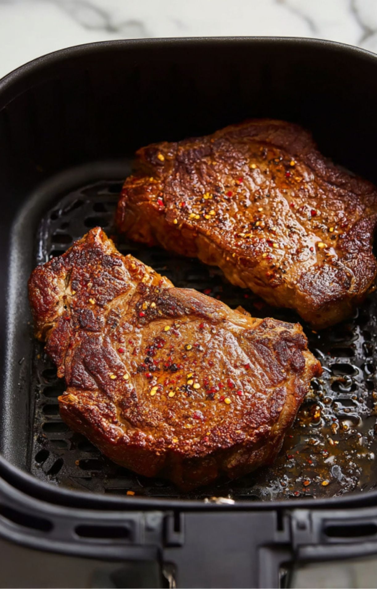 Close-up of the steaks in the air fryer basket featuring a rich, caramelized exterior and visible spices.